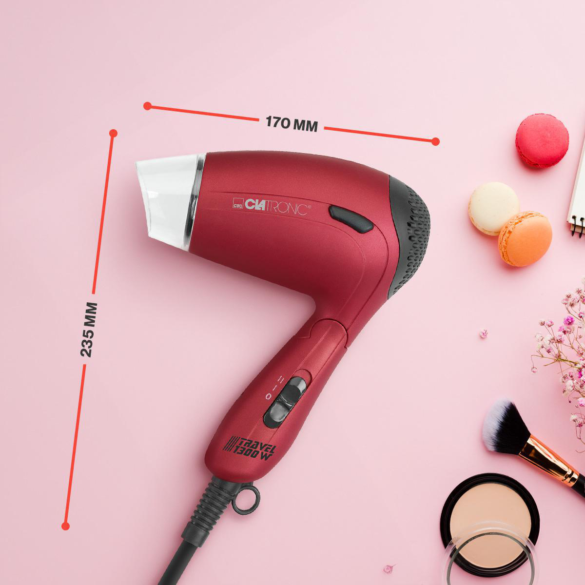 Roter Haartrockner mit Zubehör auf rosa Hintergrund. Es gibt Makronen, einen Make-up-Pinsel und Puder.