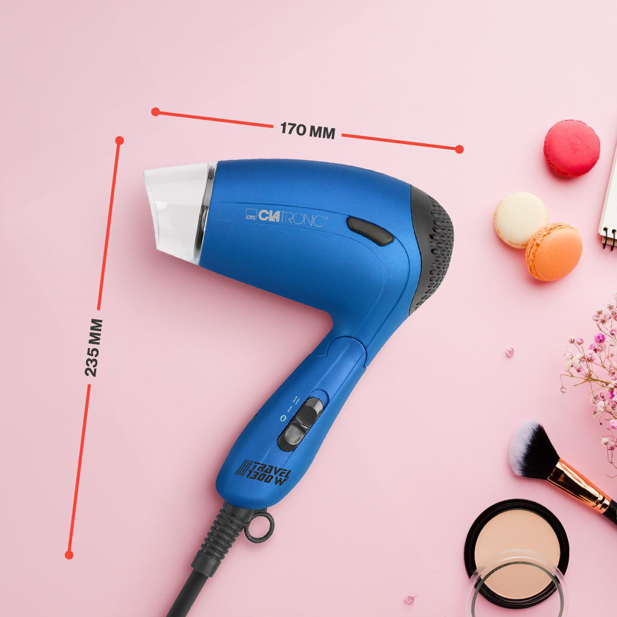 Ein blauer Fön mit Maßangaben auf pinkfarbenem Hintergrund, mit Make-up-Artikeln.