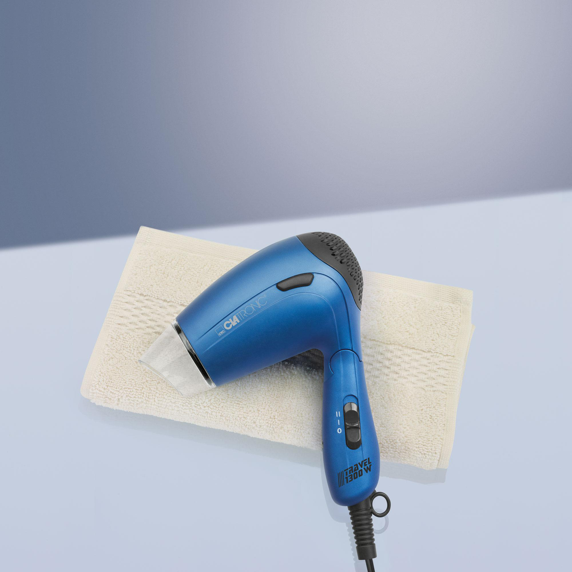 Ein blauer Fön auf einem weißen Handtuch. Der Hintergrund ist ein hellblauer Farbverlauf.