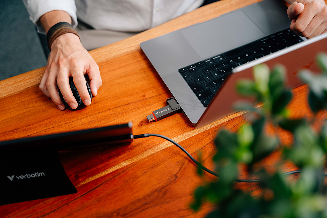 Egy kéz egeret használ egy asztalon egy laptop és egy Verbatim USB mellett.