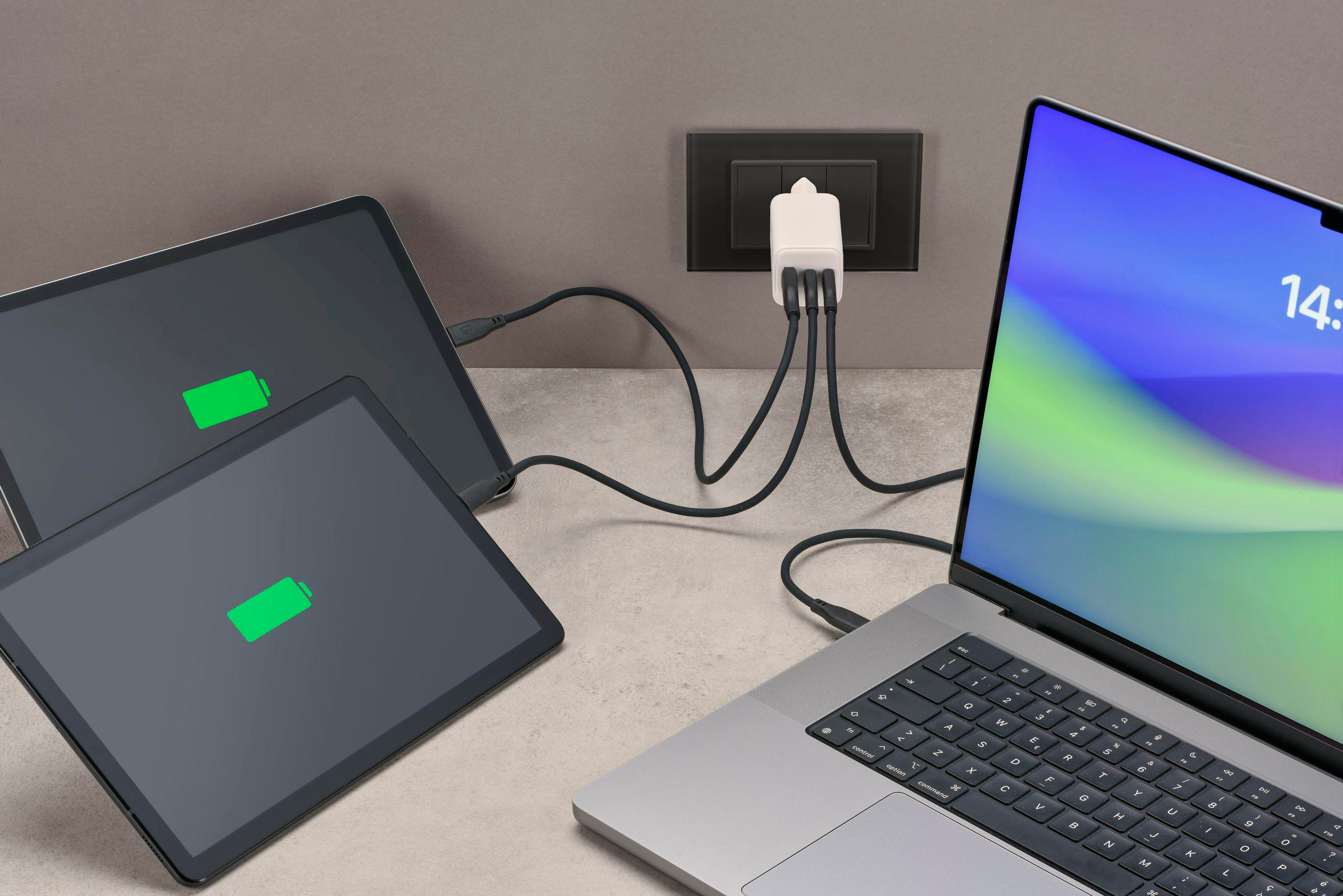 Zwei Tablets und ein Laptop werden aufgeladen. Sie sind an ein weißes Multiport-Ladegerät angeschlossen.