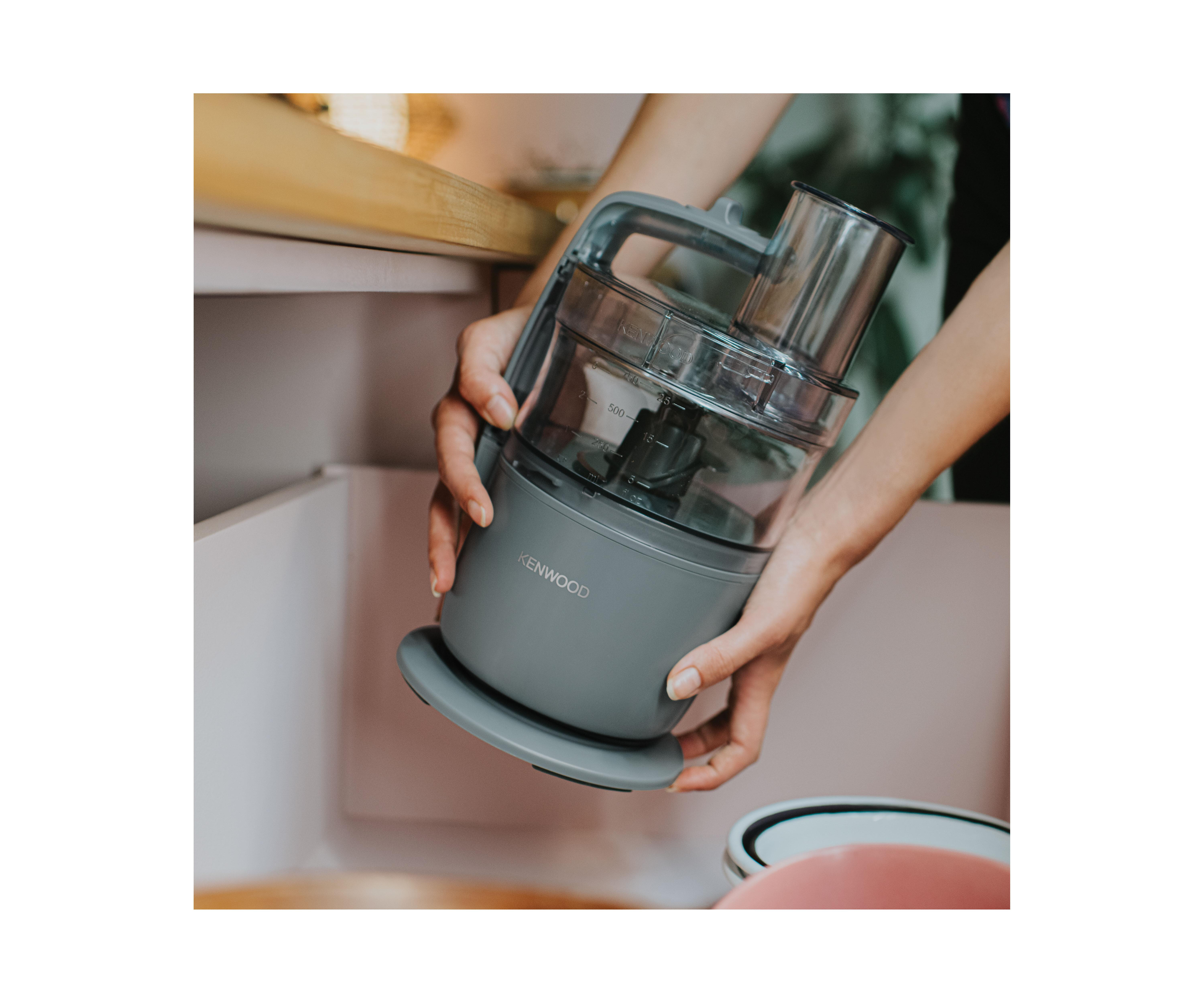 Frau hält einen grauen Küchenmixer in einem Küchenschrank.
