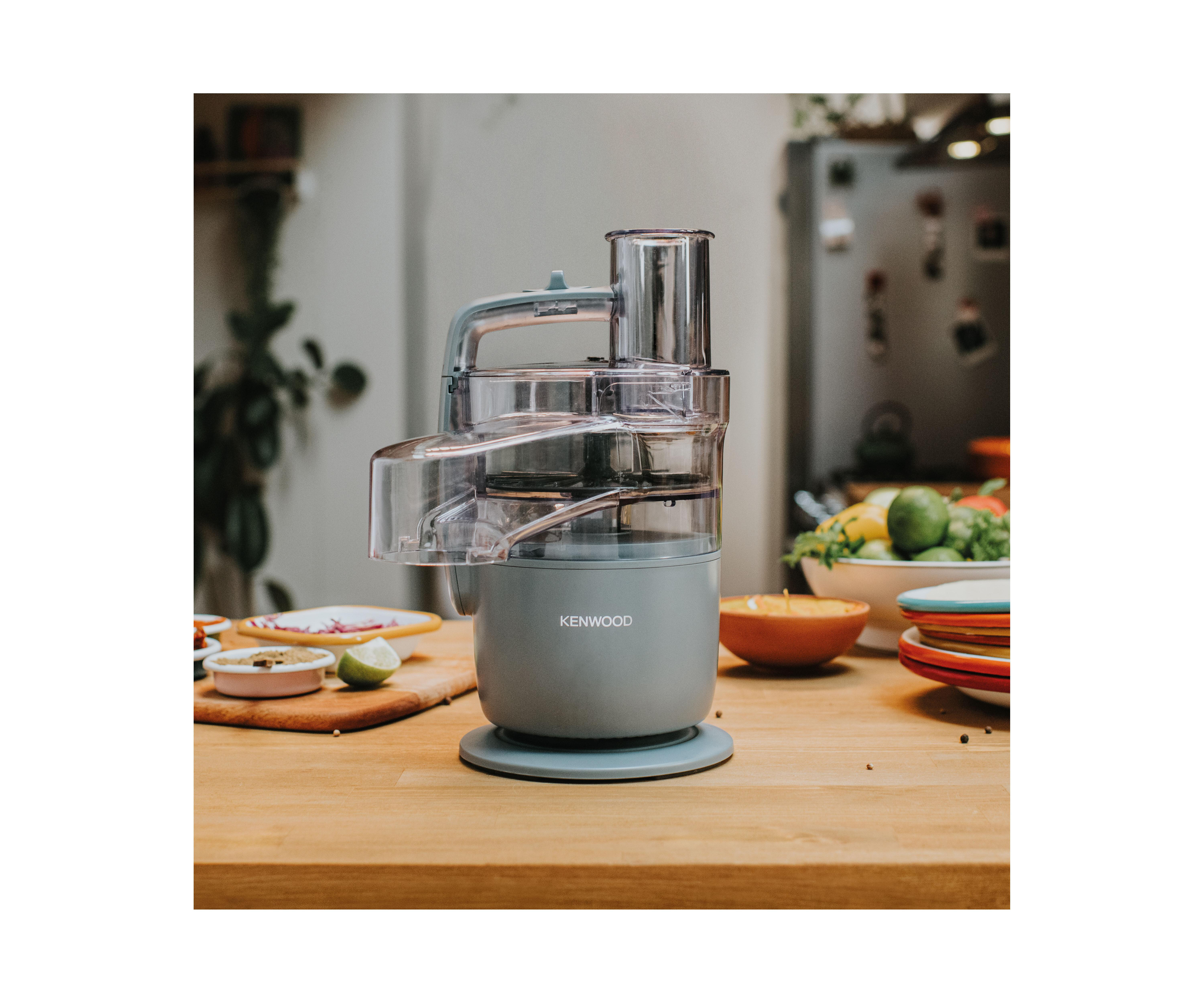 Food Processor auf einem Holztisch. Geschnittene Limette und andere Zutaten liegen auf dem Tisch.