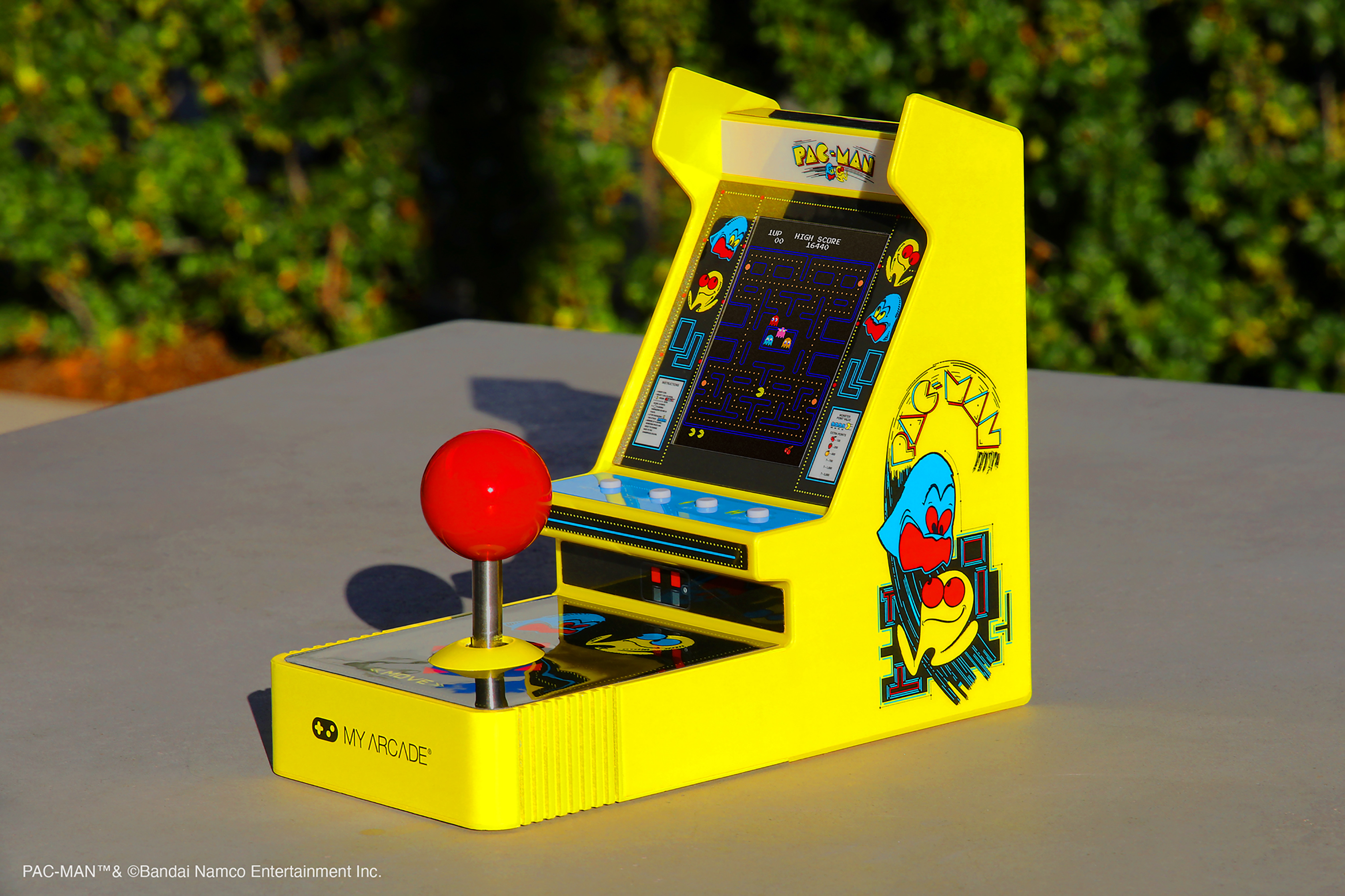 Kırmızı bir joystick'e sahip sarı bir Pac-Man atari oyunu. Oyun gri bir masada.