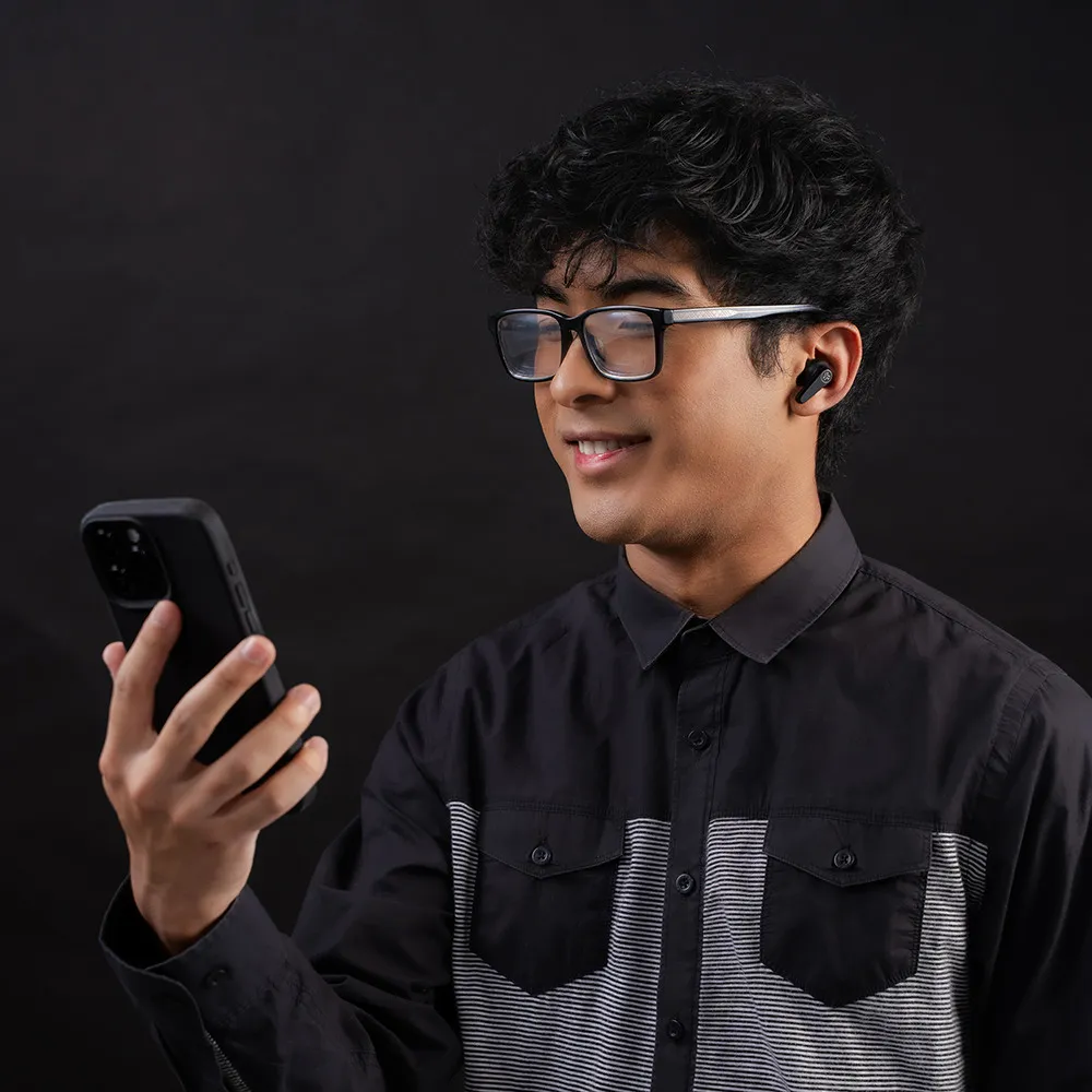 Mann mit Brille und Ohrhörern, der auf sein Telefon schaut. Schwarzes Hemd, schwarzer Hintergrund.