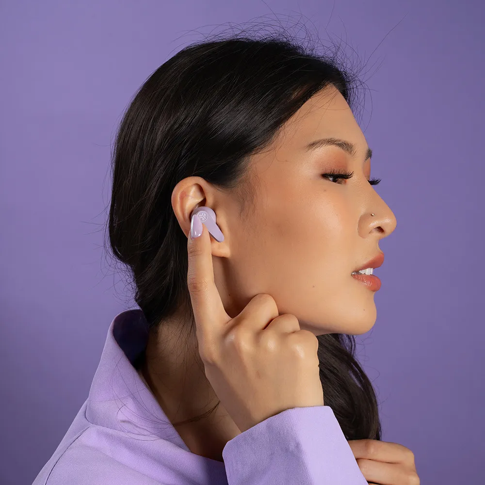 Una donna con un auricolare lo tocca con il dito. Sfondo e giacca viola.