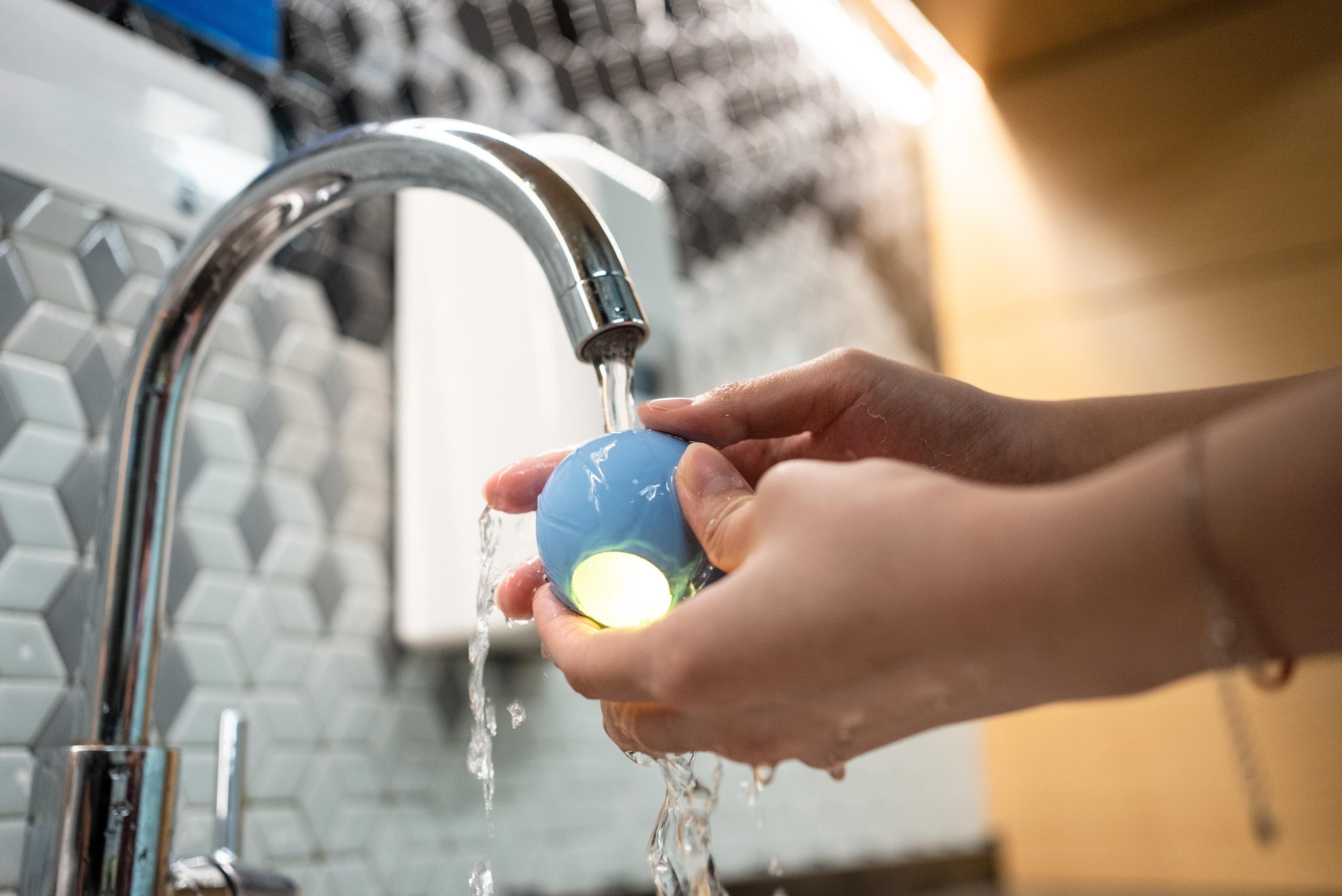 Hände waschen einen hellblauen Ball mit grünem Licht unter fließendem Wasser.
