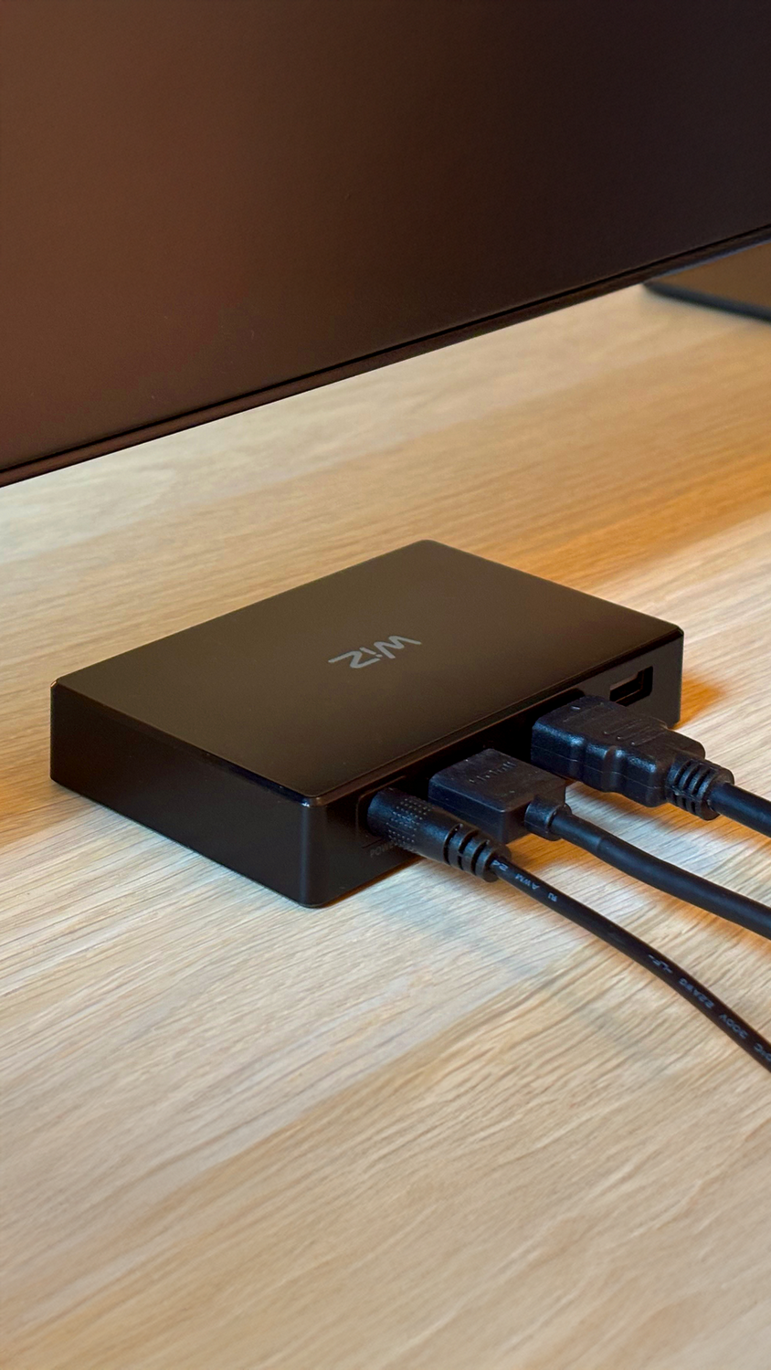 Primer plano de una caja WiZ negra con cables enchufados, sobre una superficie de madera.