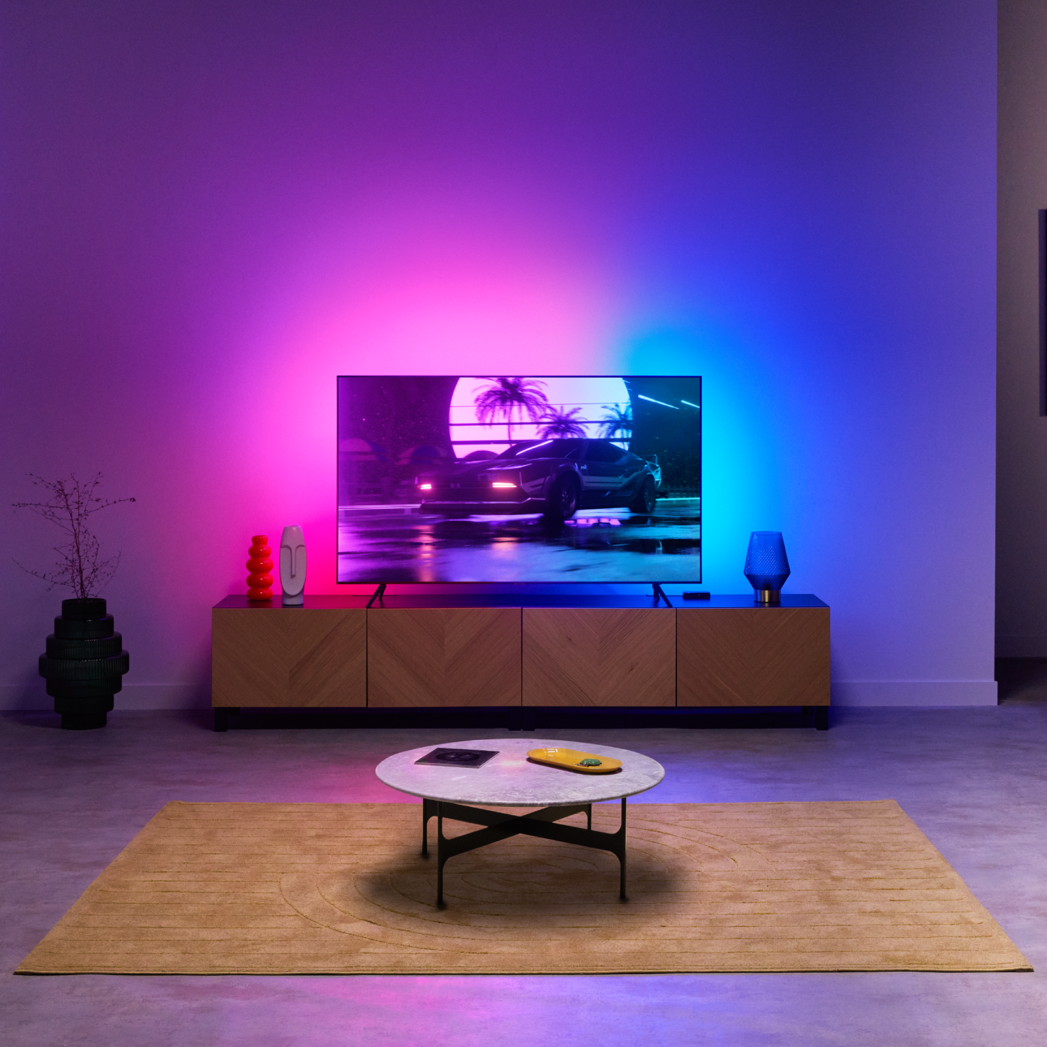 Salón con un televisor mostrando una escena de coche, con iluminación de pared azul y roja.