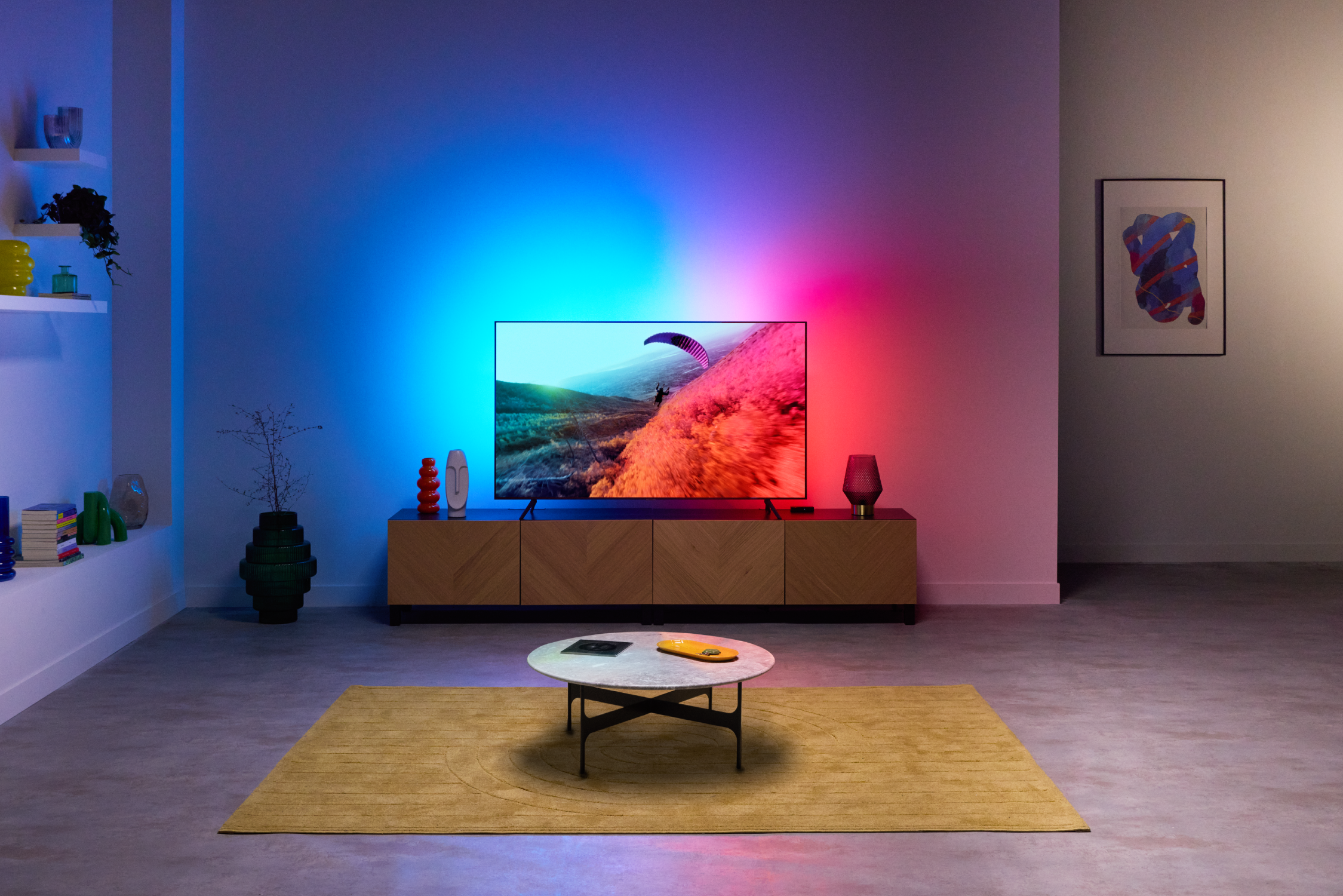 Salón con un televisor mostrando una escena de parapente, con iluminación de pared azul y roja.