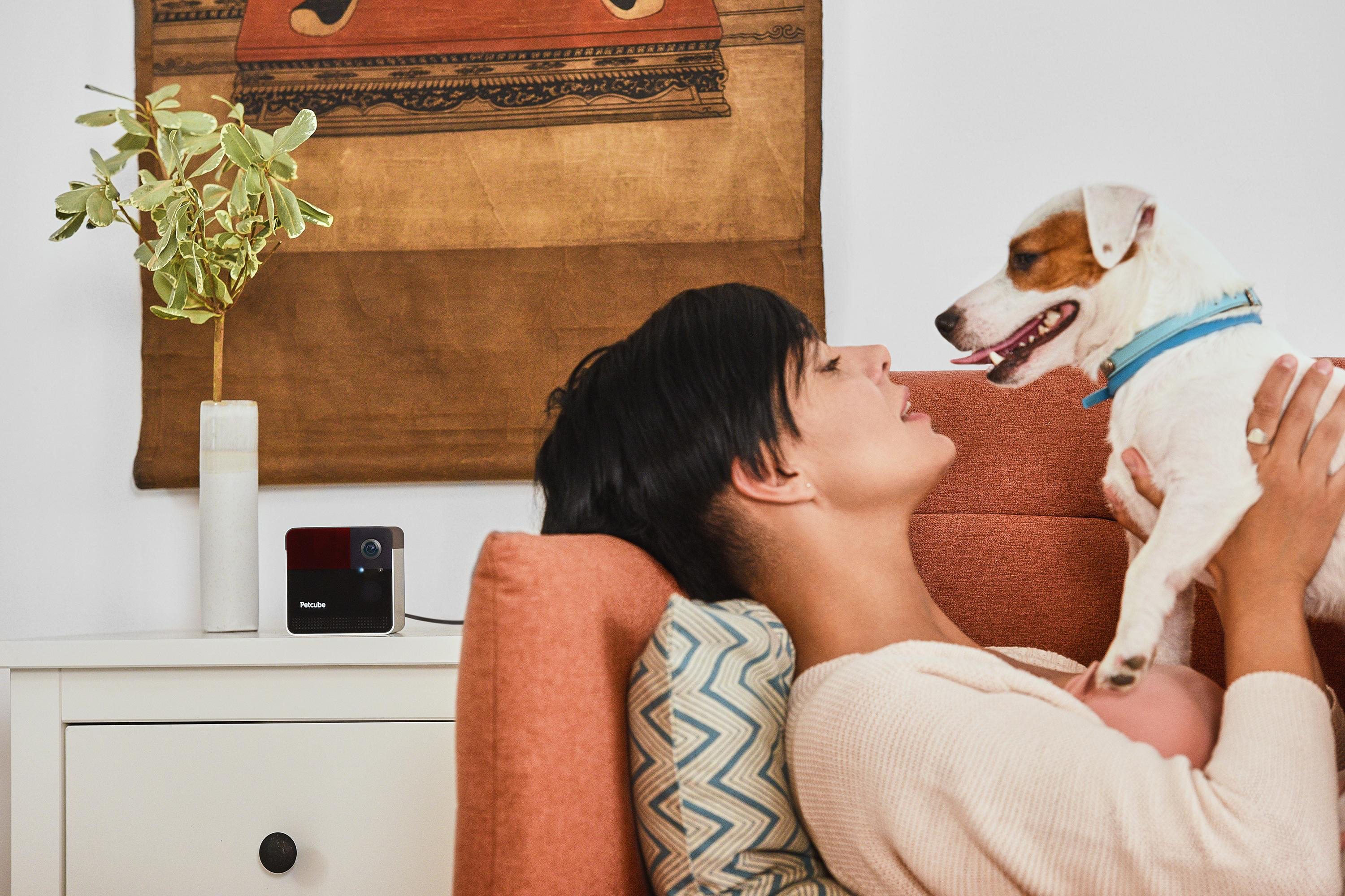 Eine Frau liegt auf einem Sofa mit einem Hund. Ein schwarz-rotes Gerät ist sichtbar.
