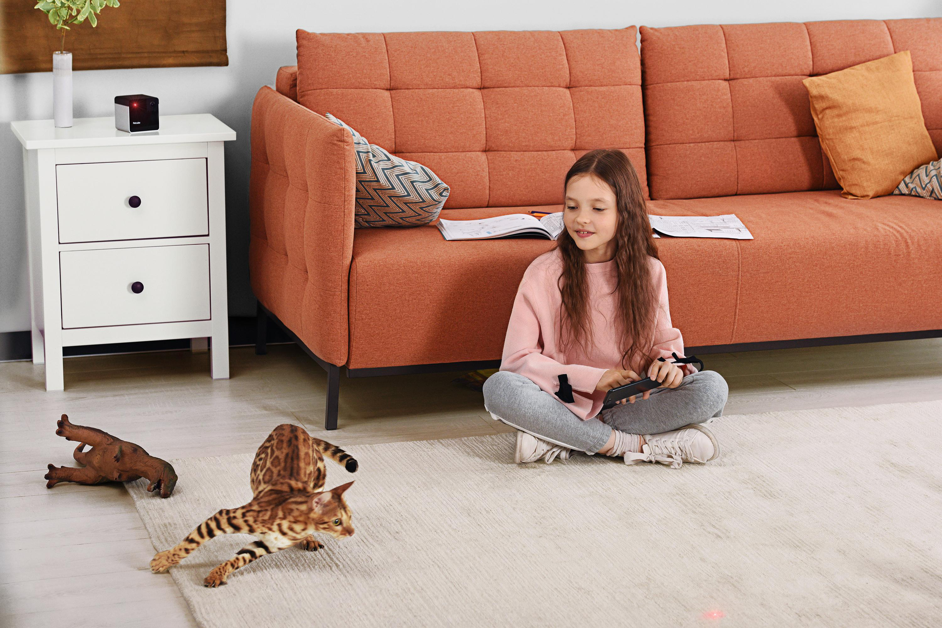 Ein Mädchen sitzt am Boden mit Fernbedienung, Katzen spielen in der Nähe.