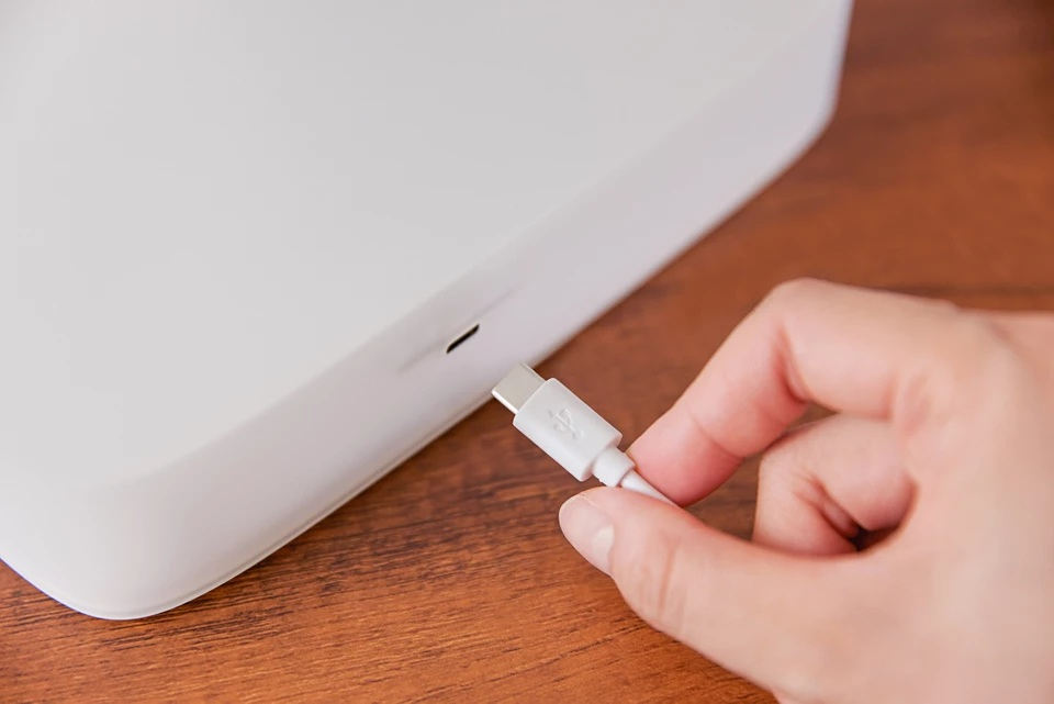 Ręka trzyma kabel USB-C. Kabel jest podłączony do białego urządzenia.