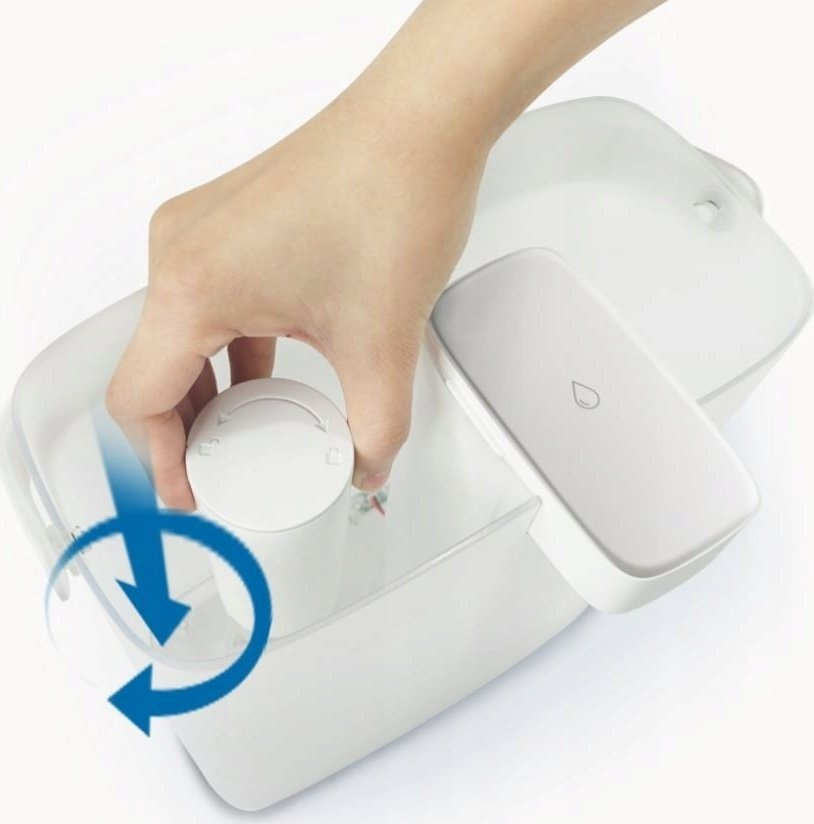 Dłoń przekręca pokrętło w białym systemie filtracji wody. Niebieska strzałka wskazuje kierunek.