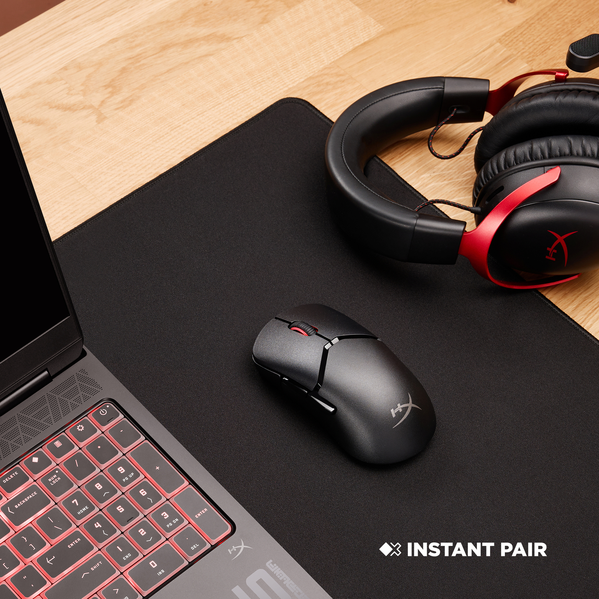 A laptop, mouse, and headset are on a desk. The headset is red and black.