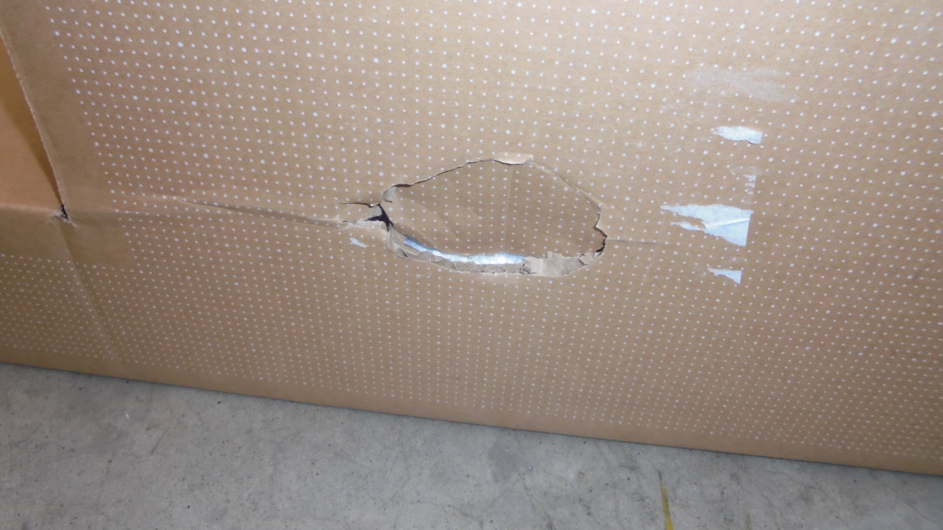 Uszkodzone pudełko kartonowe z dużą dziurą pośrodku. Brązowy kolor z białymi kropkami.