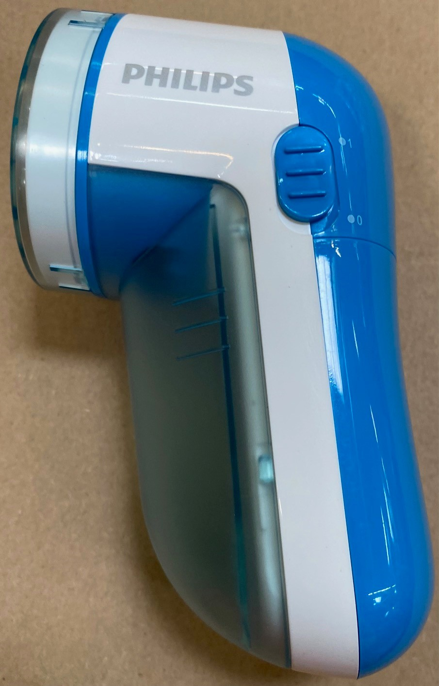 Niebiesko-biała golarka do tkanin Philips. Posiada przezroczysty pojemnik na wióry z tkaniny.