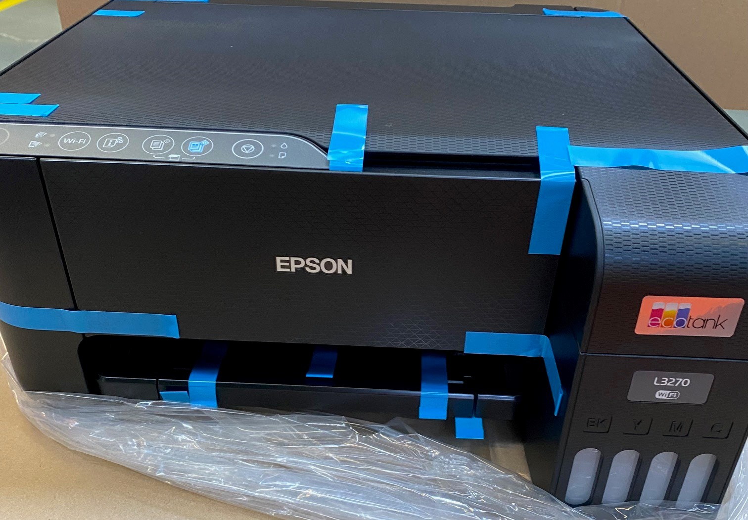 Czarna drukarka Epson z niebieską taśmą. Widok z góry. Widoczne ikony Wi-Fi i inne.