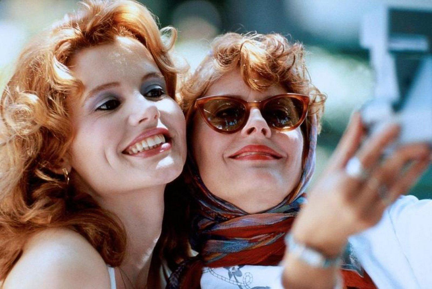 Zwei Frauen lächeln, eine hält ein Telefon für ein Selfie. Beide haben rotes Haar.