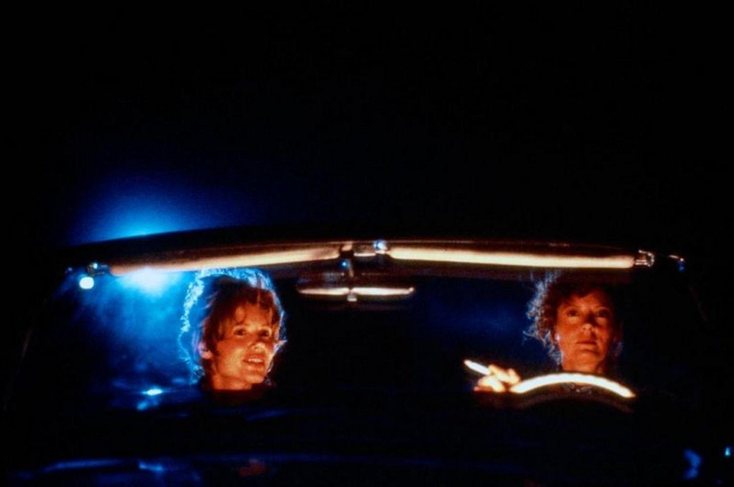 Zwei Personen in einem Auto bei Nacht. Einer raucht, der andere schaut nach vorn.