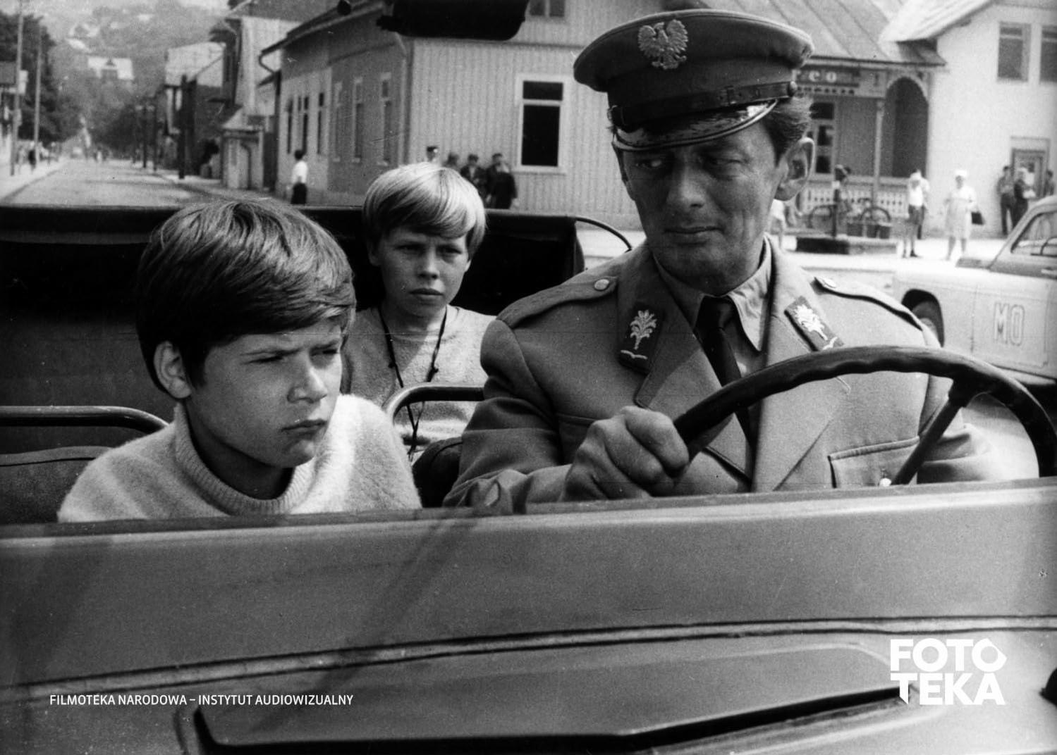 Zwei Jungen und ein Mann in einem Auto. Der Mann in Uniform fährt; die Jungen schauen aus dem Fenster.