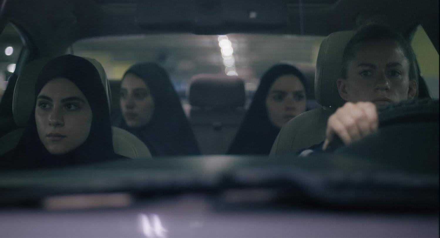 Vier Frauen sind in einem Auto. Sie schauen in einer schwach beleuchteten Parkgarage nach vorne.