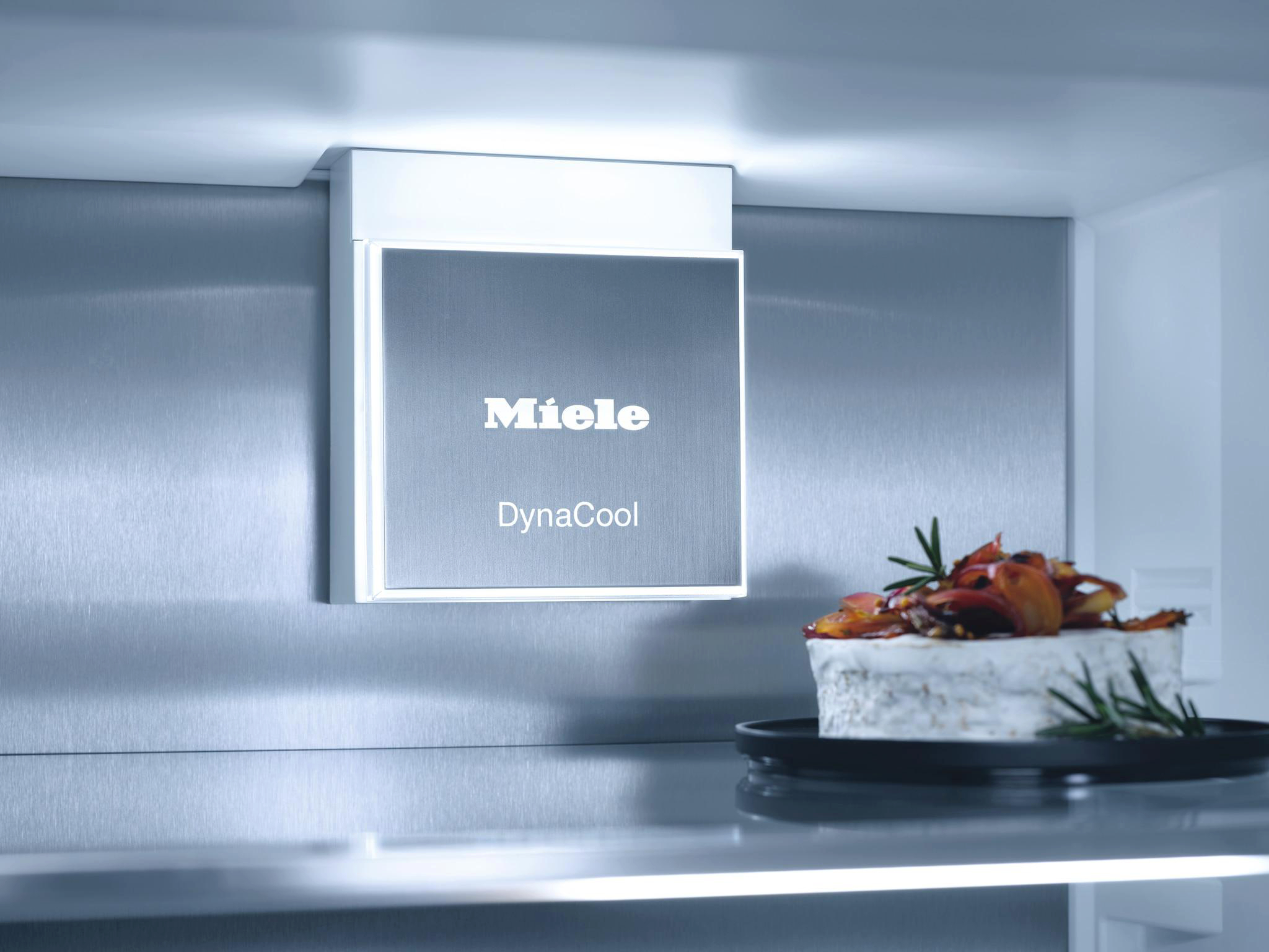 Eine Miele DynaCool-Einheit in einem Kühlschrank. Eine Platte mit Essen daneben.
