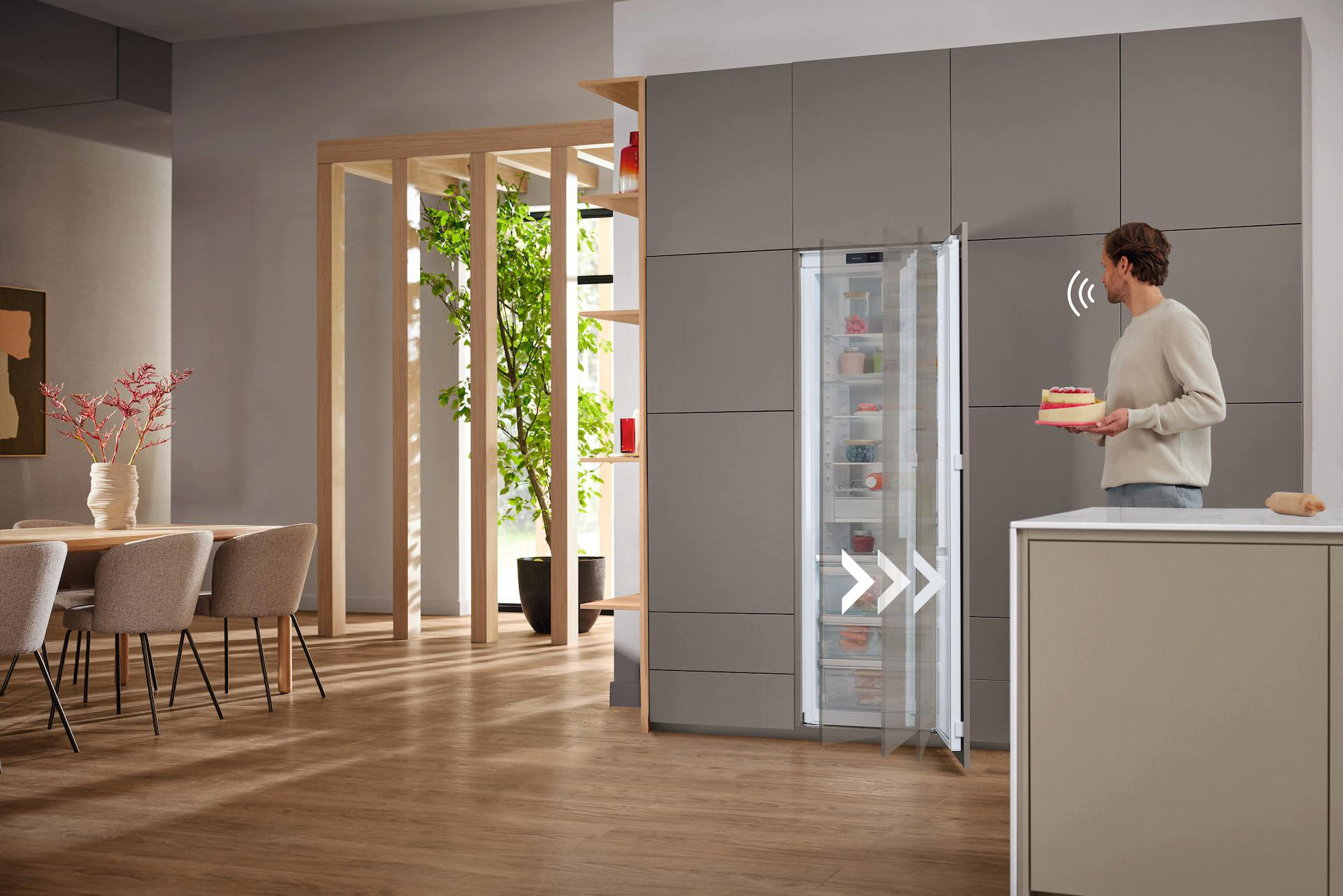 Ein Mann öffnet einen Miele-Kühlschrank in einer modernen Küche. Ein Kuchen in der Hand.