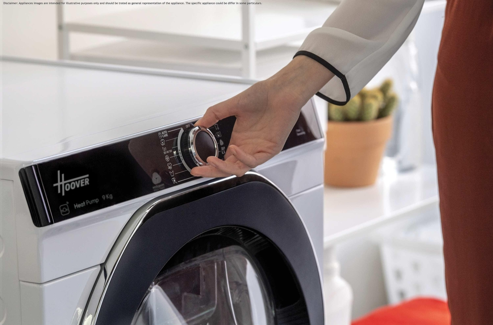 Bir kişinin eli beyaz bir Hoover kurutma makinesinin kadranını çeviriyor. Arka planda saksıda bir kaktüs var.