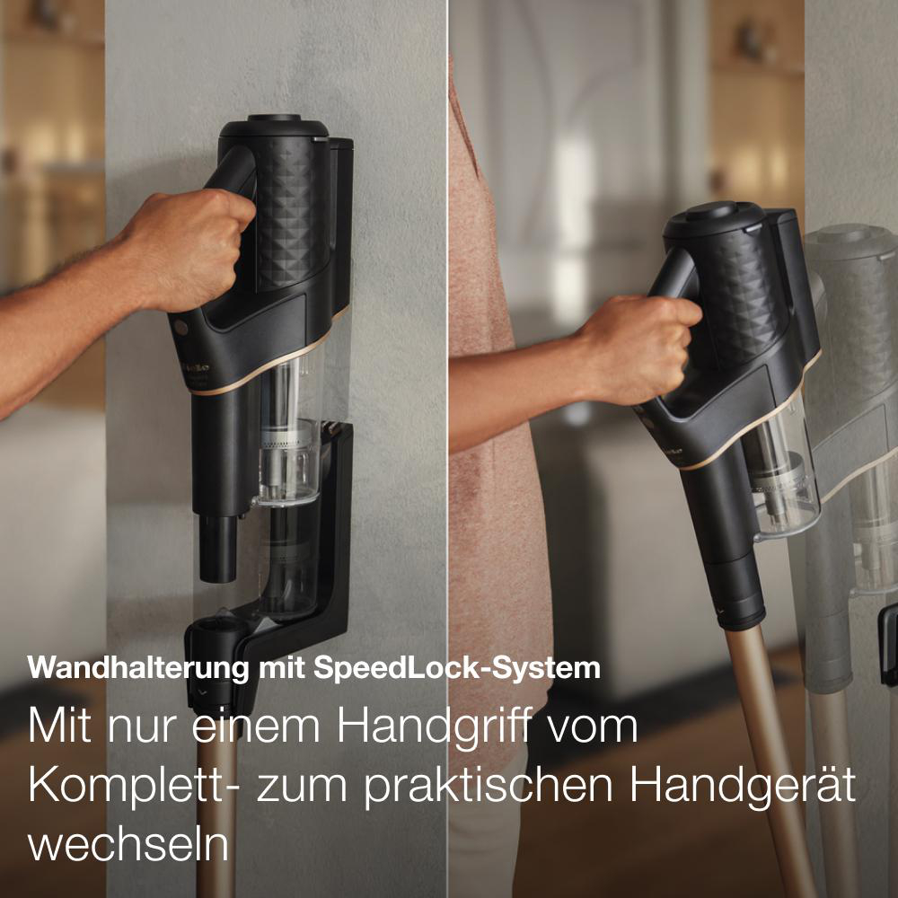 Staubsauger an der Wandhalterung. Person hält ihn. Goldakzente.