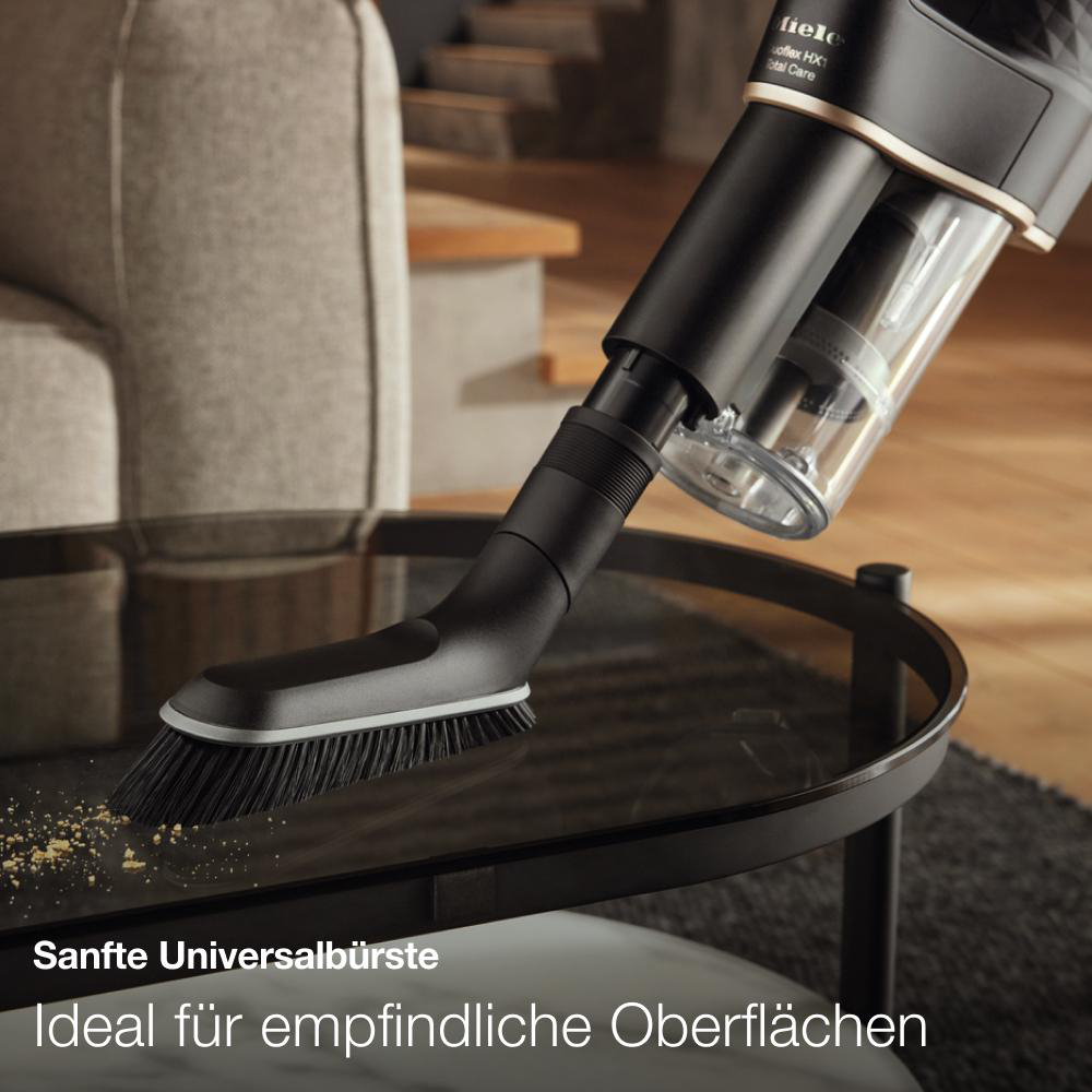 Staubsauger reinigt Tisch. Bürstenkopf und Schmutz sichtbar.
