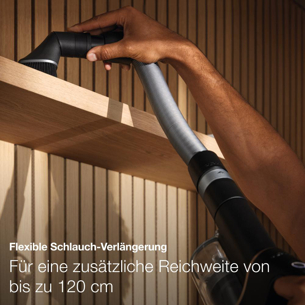Staubsauger mit Verlängerung. Person hält ihn. Holzvertäfelung im Hintergrund.