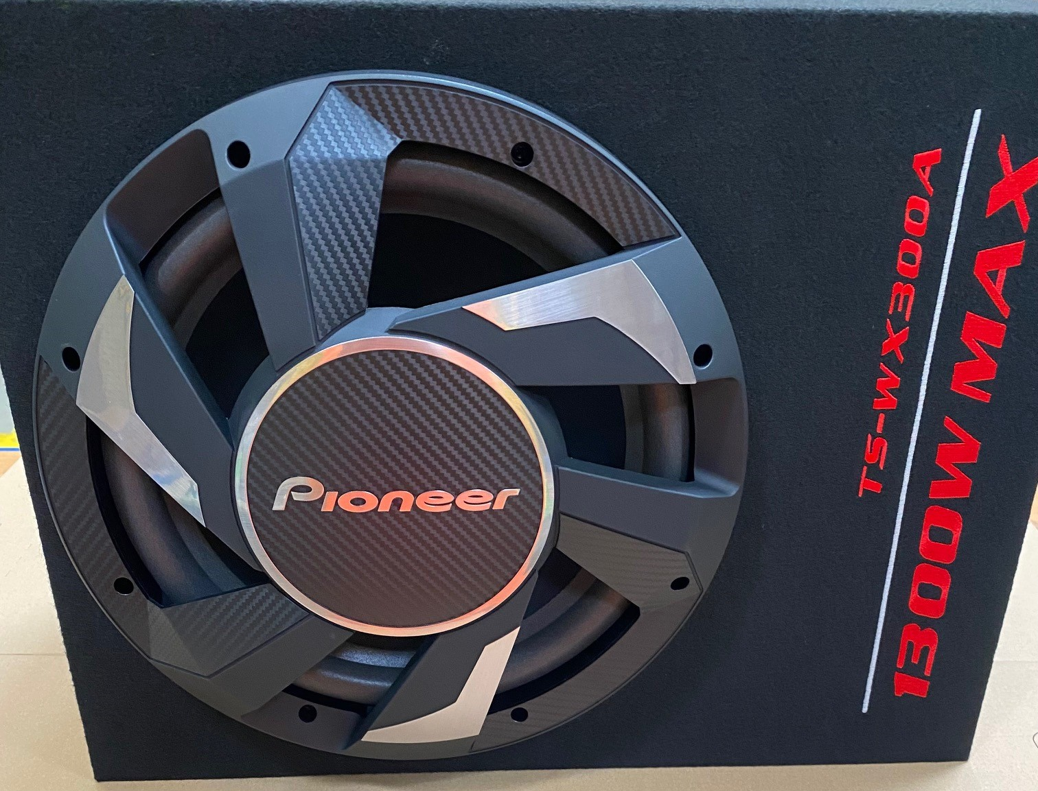 Czarny subwoofer Pioneer z włóknem węglowym, srebrnymi akcentami i czerwonym napisem '1300W MAX'.
