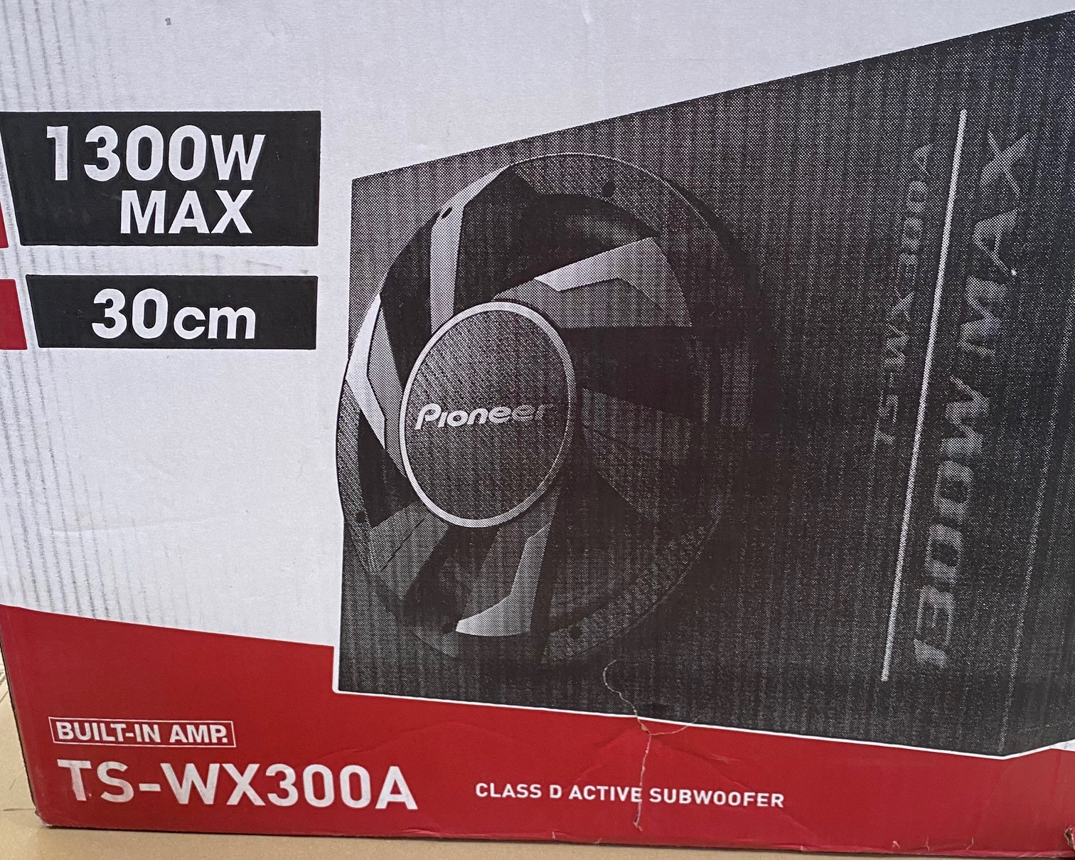 Pudełko subwoofera Pioneer. Kolory czarny i czerwony. Tekst: 1300W Max, 30cm, TS-WX300A. Wbudowany wzmacniacz. Aktywny subwoofer klasy D.