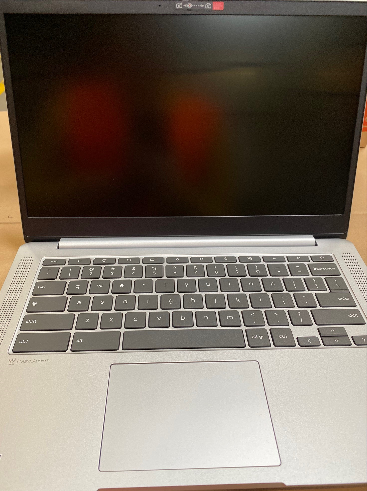 Otwarty srebrny laptop z czarnym ekranem. Widoczna klawiatura i touchpad. Ekran posiada kamerę internetową.