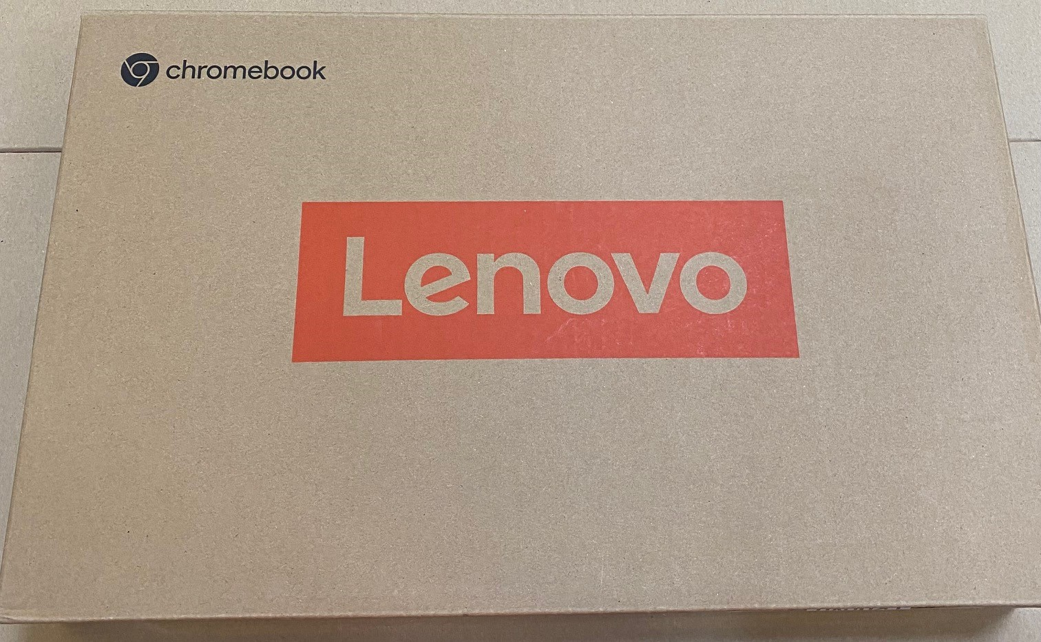 Pudełko Lenovo Chromebook. Pudełko jest beżowe z czerwonym prostokątem z logo Lenovo. Widoczne jest słowo 'chromebook'.