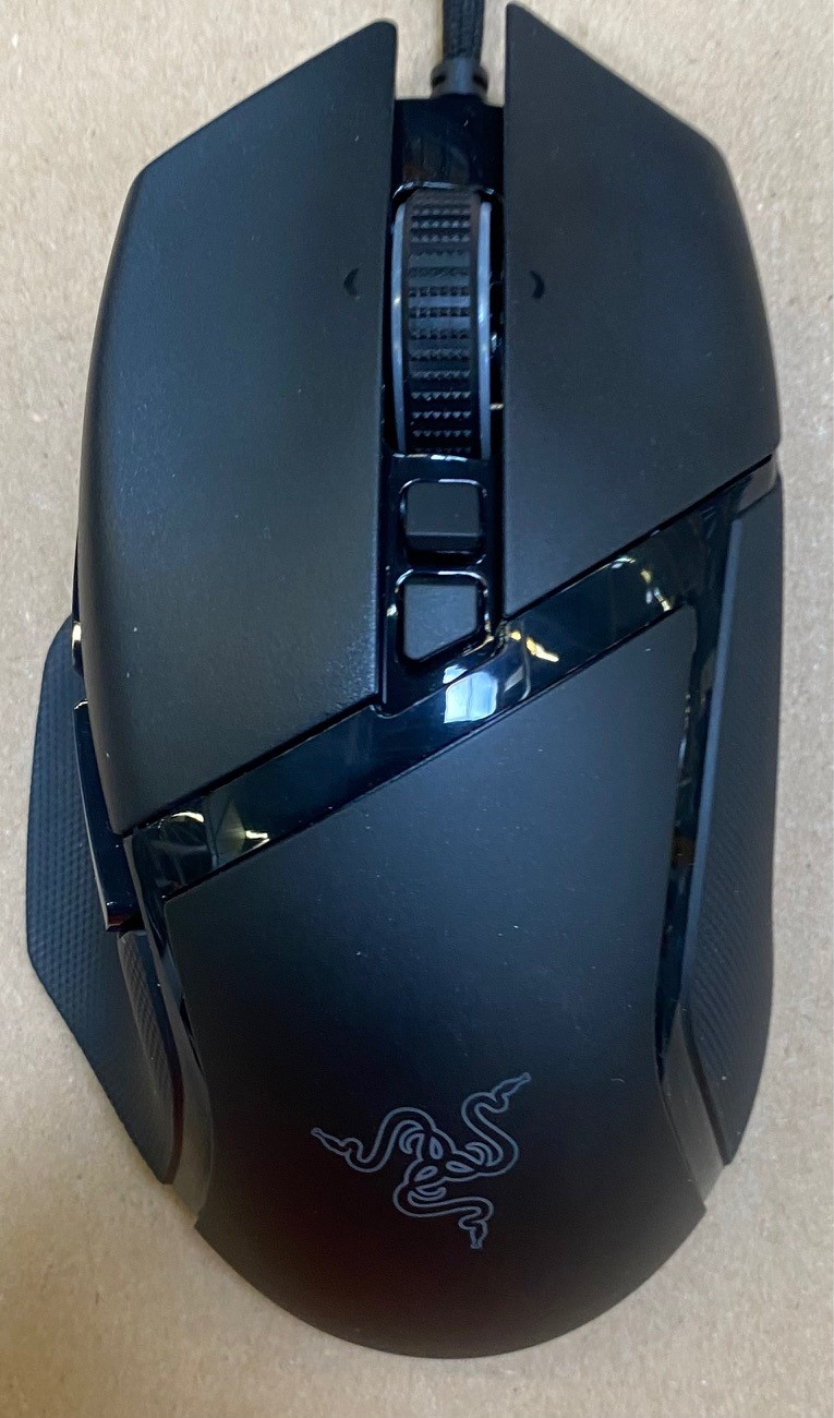 Czarna mysz komputerowa Razer na jasnobrązowej powierzchni. Posiada kółko, przyciski i logo Razer.