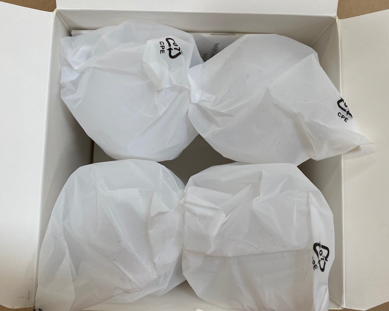 Cztery białe paczki zapakowane w plastik w białym pudełku. Każda paczka ma symbol recyklingu CPE.