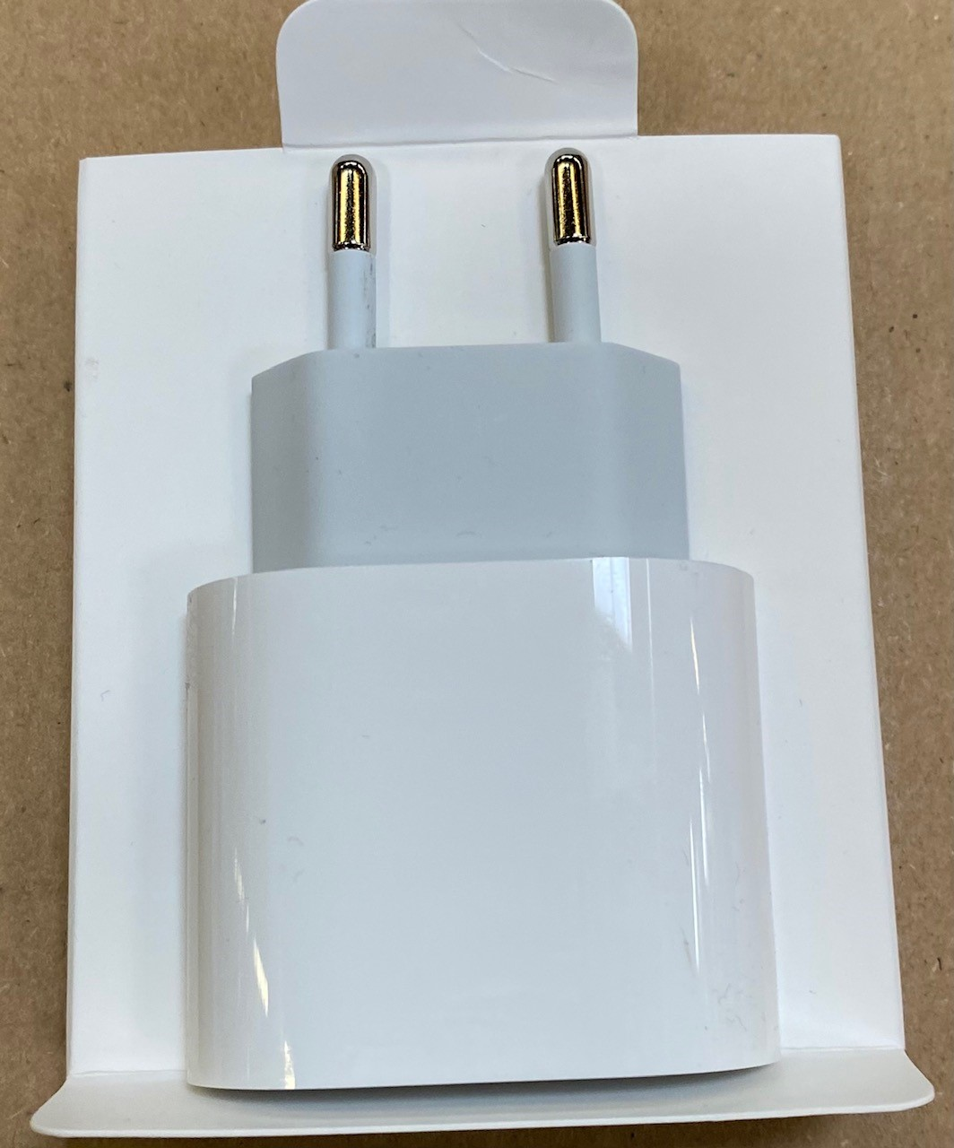 Biała ładowarka Apple w opakowaniu na drewnianej powierzchni.