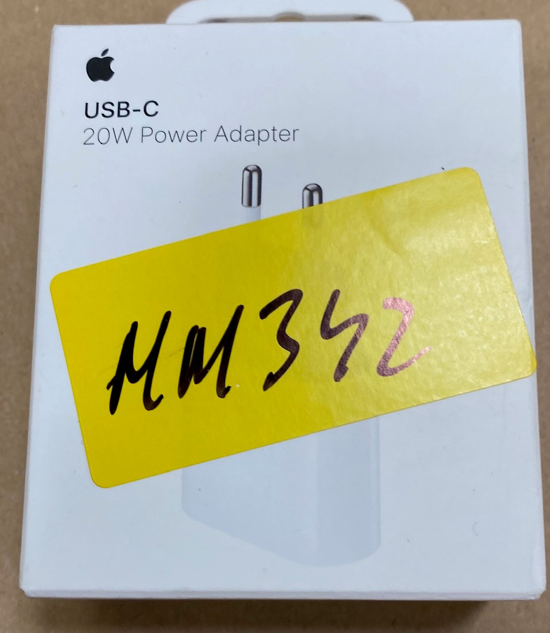 Białe pudełko ładowarki Apple z żółtą naklejką i pismem odręcznym.