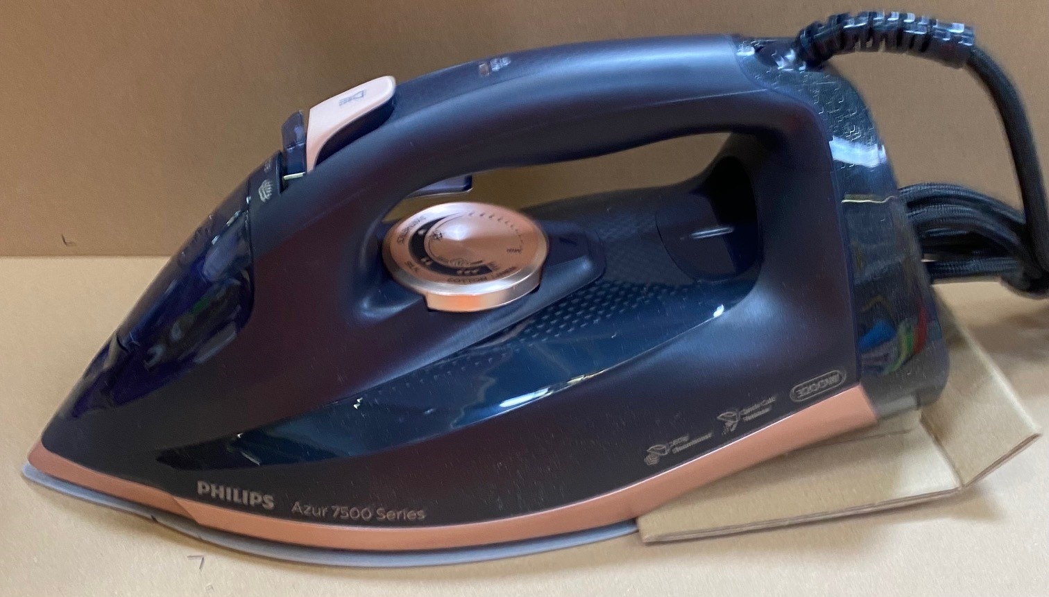 Czarno-miedziane żelazko Philips Azur 7500 na kartonie. Posiada pokrętło, uchwyt i przewód.