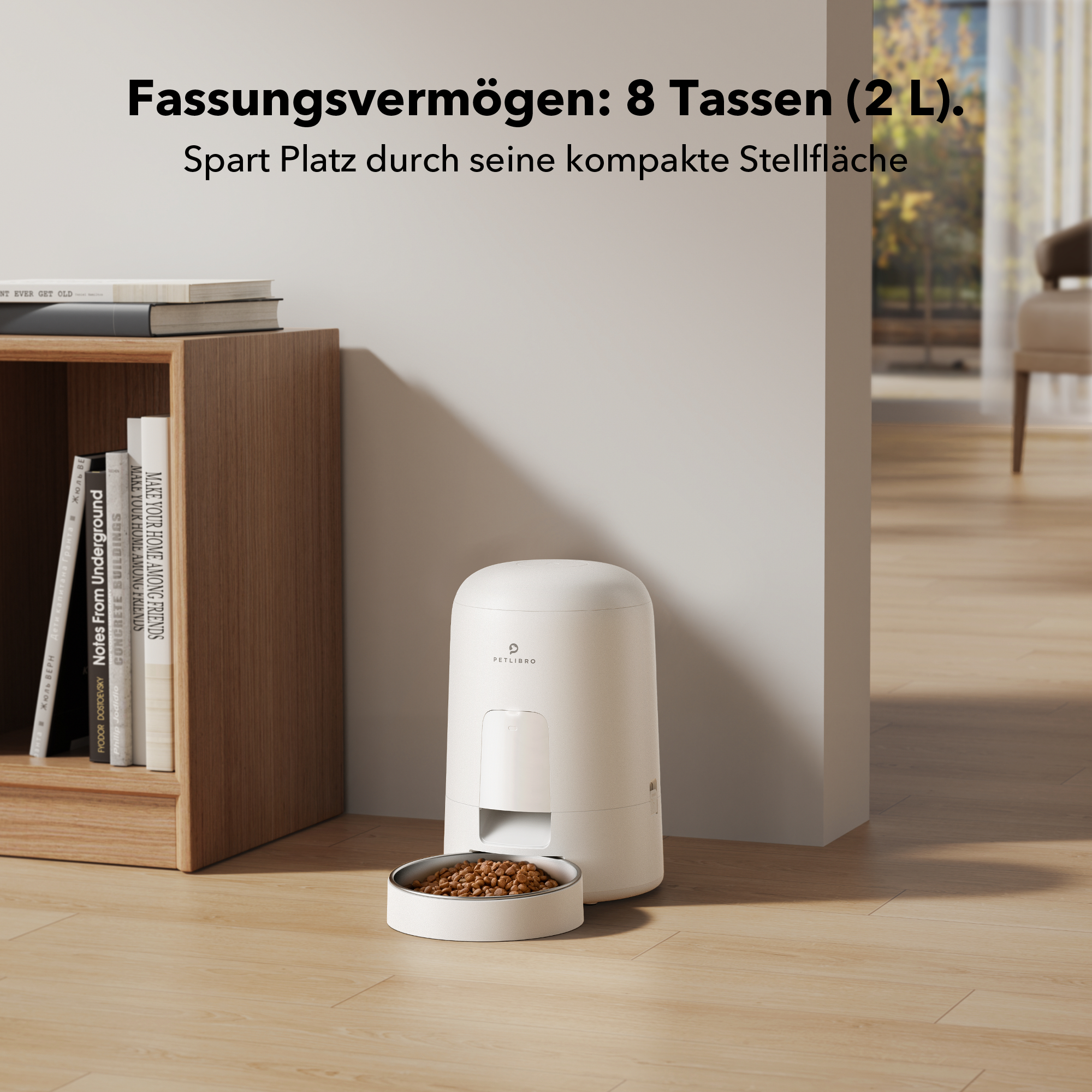 Weißer Futterautomat mit Futternapf und Büchern. Text auf Deutsch über Kapazität. Holzregal.