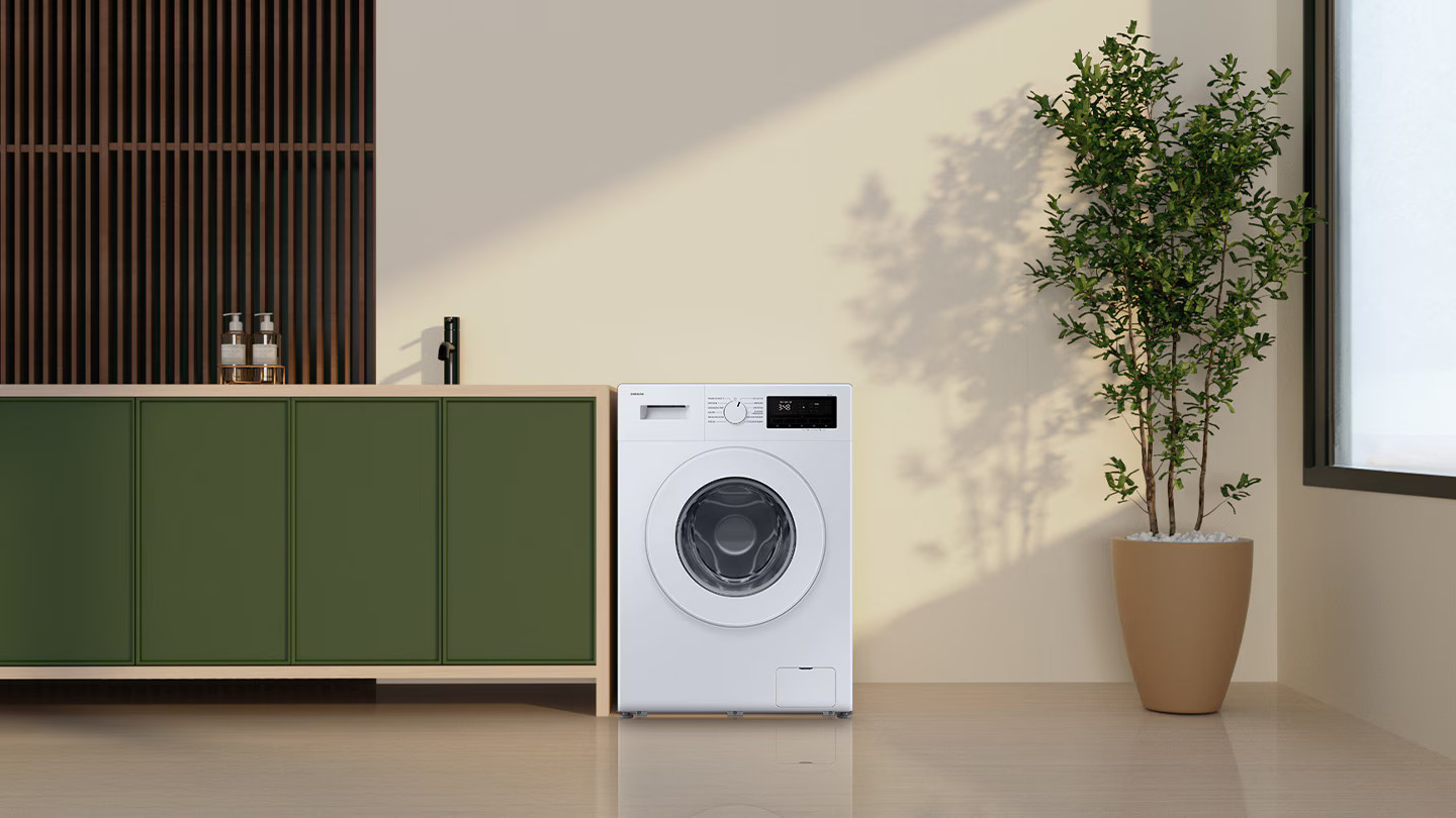 Biała pralka stoi obok zielonej szafki i rośliny w doniczce. Drewniane listwy są na ścianie.