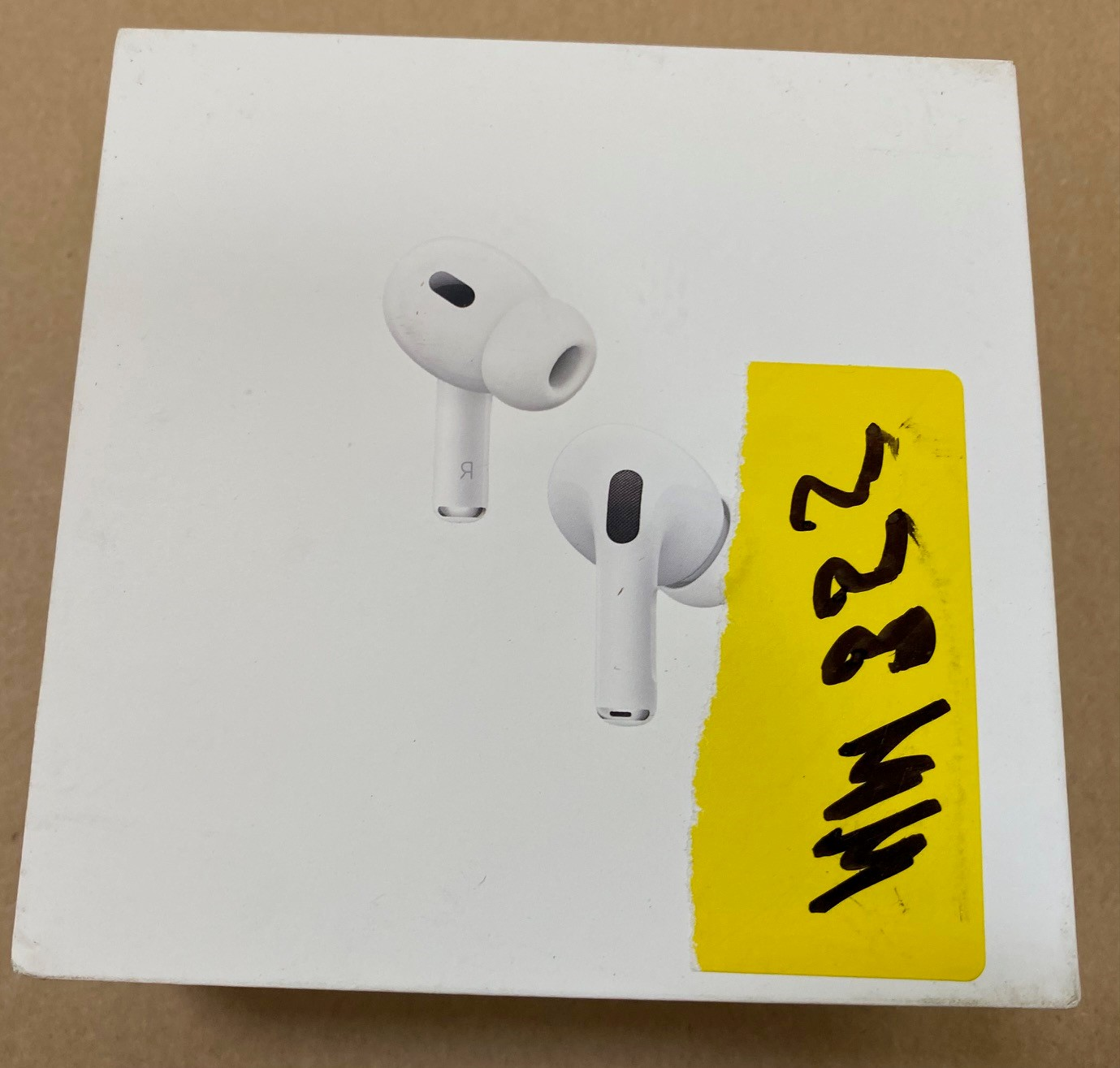 Białe etui AirPods Pro, dwa słuchawki i żółta naklejka z czarnym, ręcznie pisanym tekstem.
