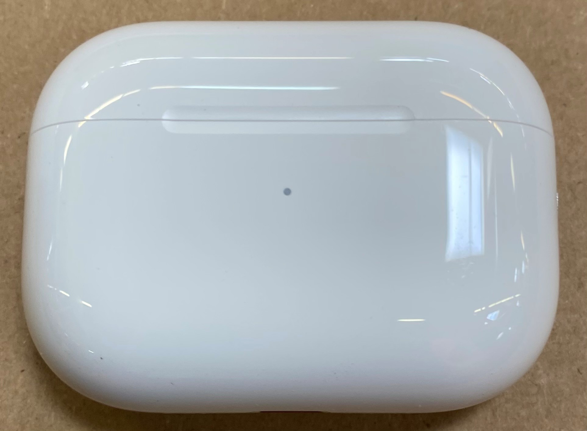 Białe etui ładujące AirPods Pro, zamknięte, na brązowej powierzchni.
