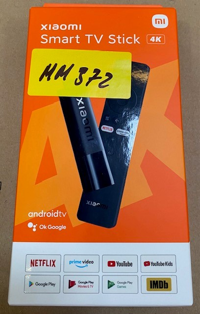 Pomarańczowe pudełko z Xiaomi TV Stick, 4K, Android TV i obrazem pilota. Żółta naklejka z "MM 372".