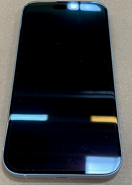 Srebrny iPhone z czarnym ekranem leży na jasnobrązowej powierzchni. Ekran odbija światło.