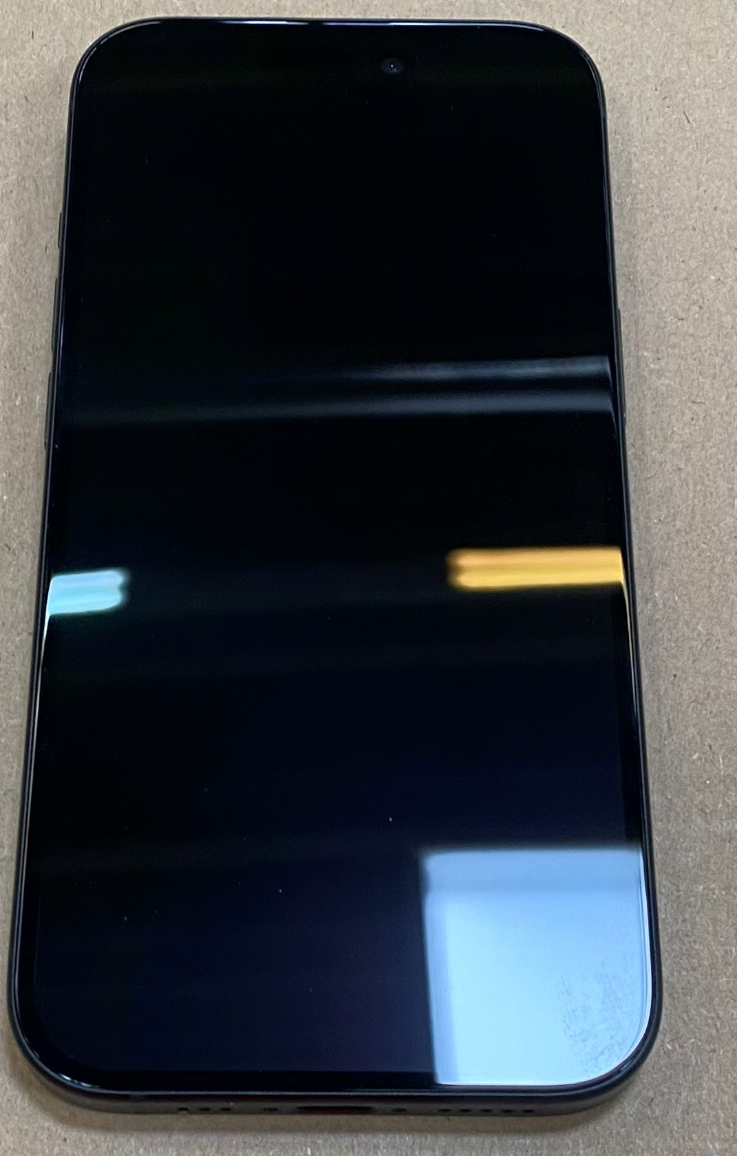 Czarny telefon na powierzchni. Ekran jest czarny, odbija światło. Powierzchnia jest jasnobrązowa.