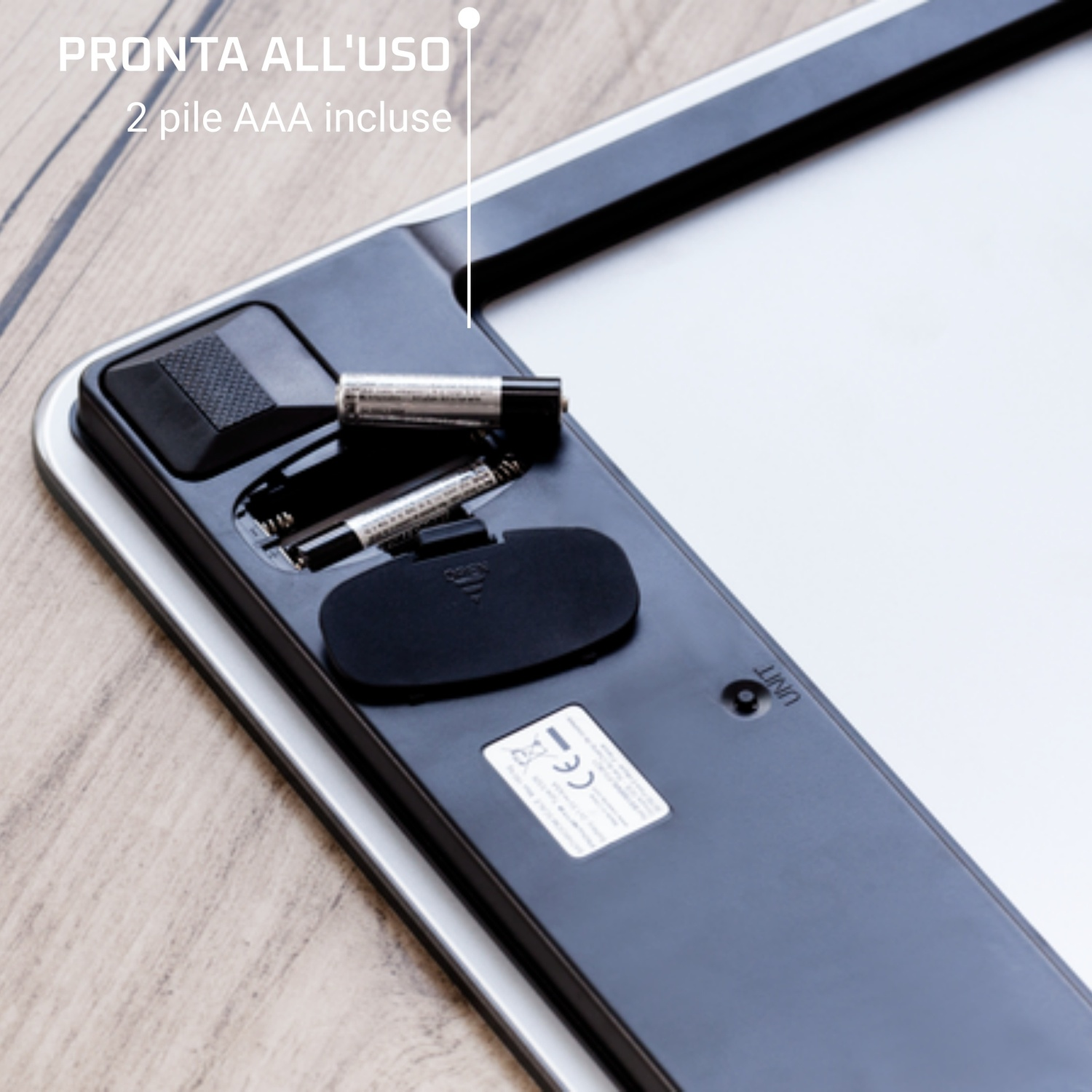 Primo piano della base di un dispositivo con vano batteria aperto, due batterie AAA inserite su tavolo di legno.