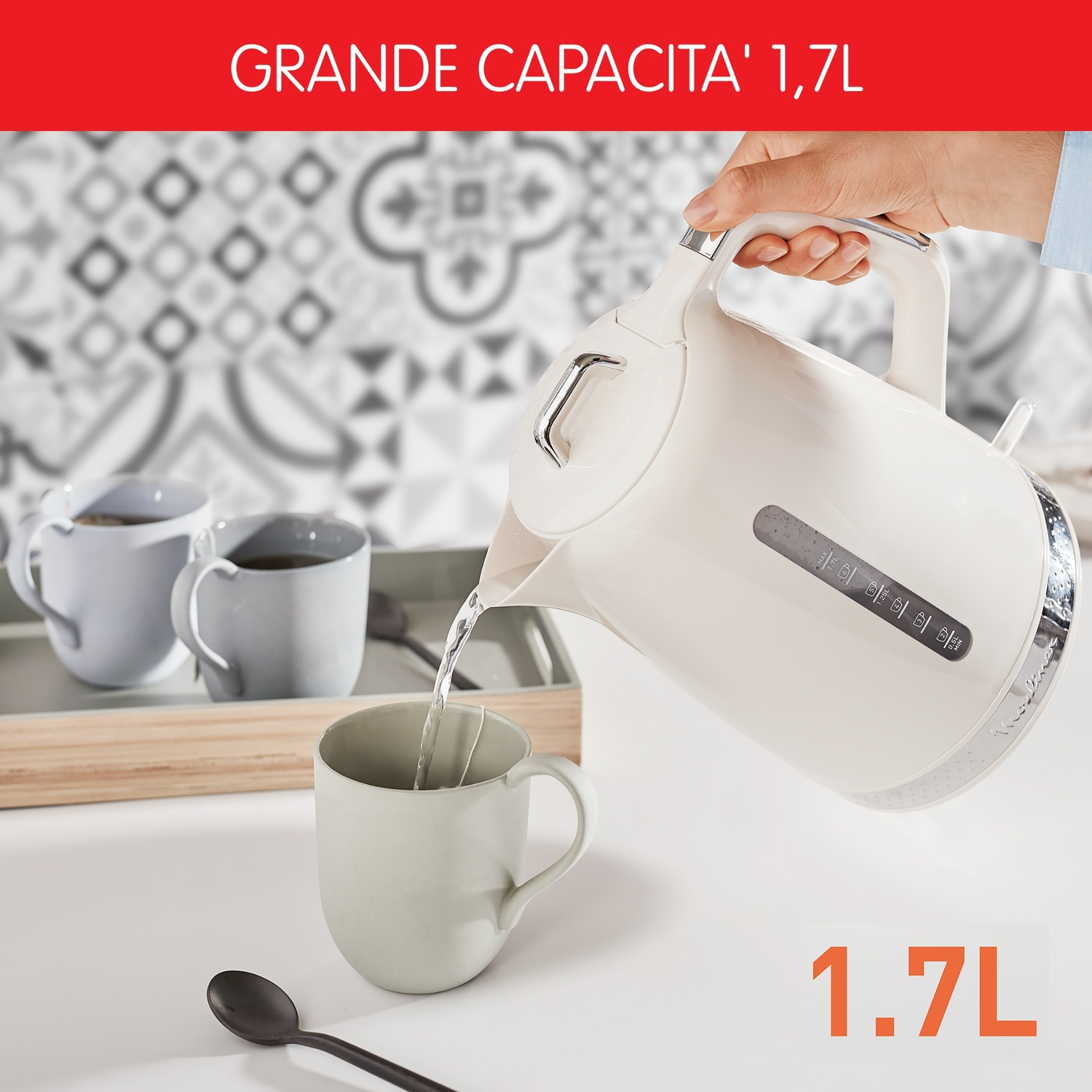 Bollitore che versa acqua in una tazza. Due tazze su un vassoio sullo sfondo, un cucchiaio e una parete a motivi.